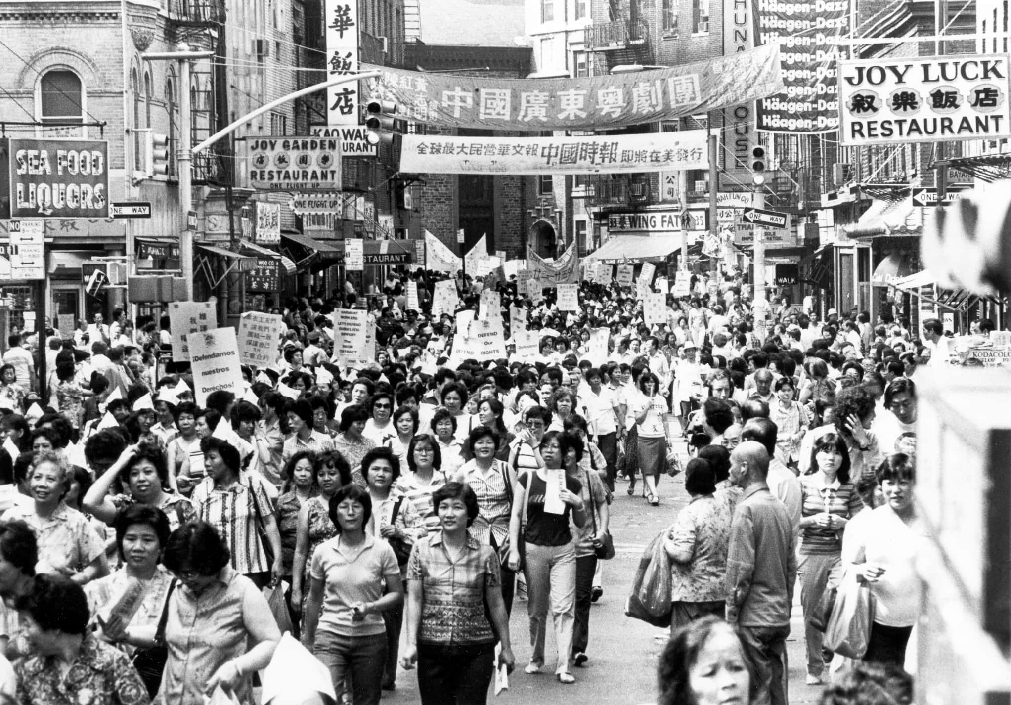 Large crowd of people march through Chinatown street.