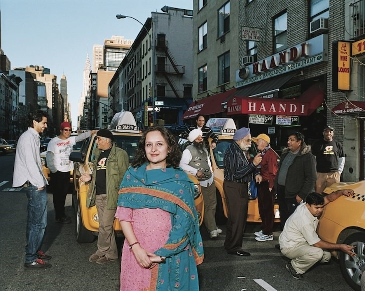 Bhairavi Desa wearing a sari poses in front of a group of taxi drivers parked on a city street.