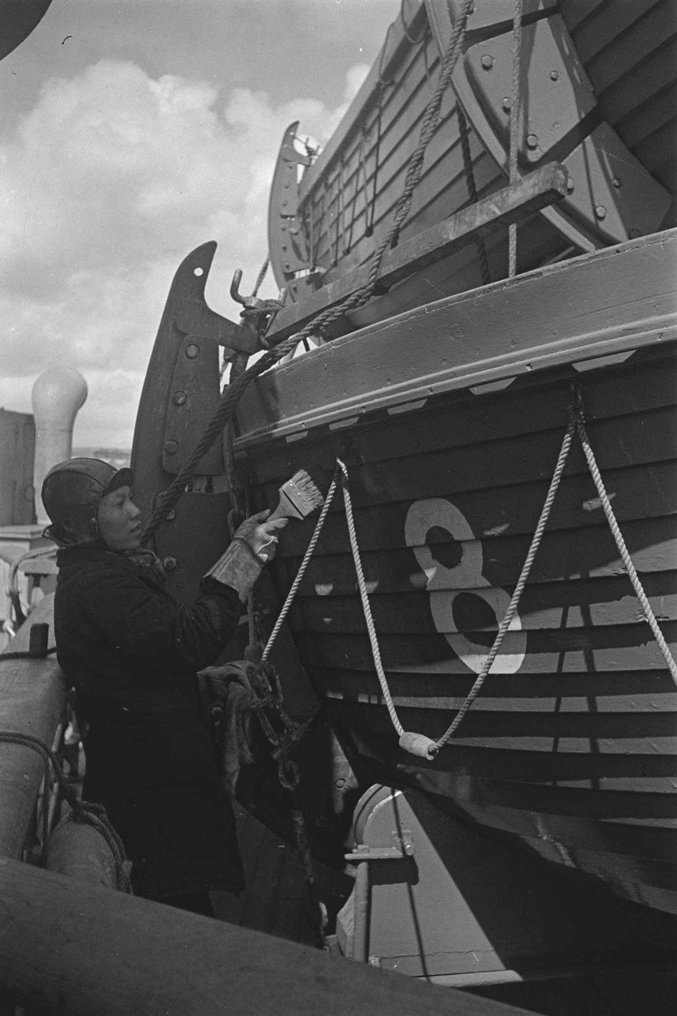 A worker paints the side of a docked boat.