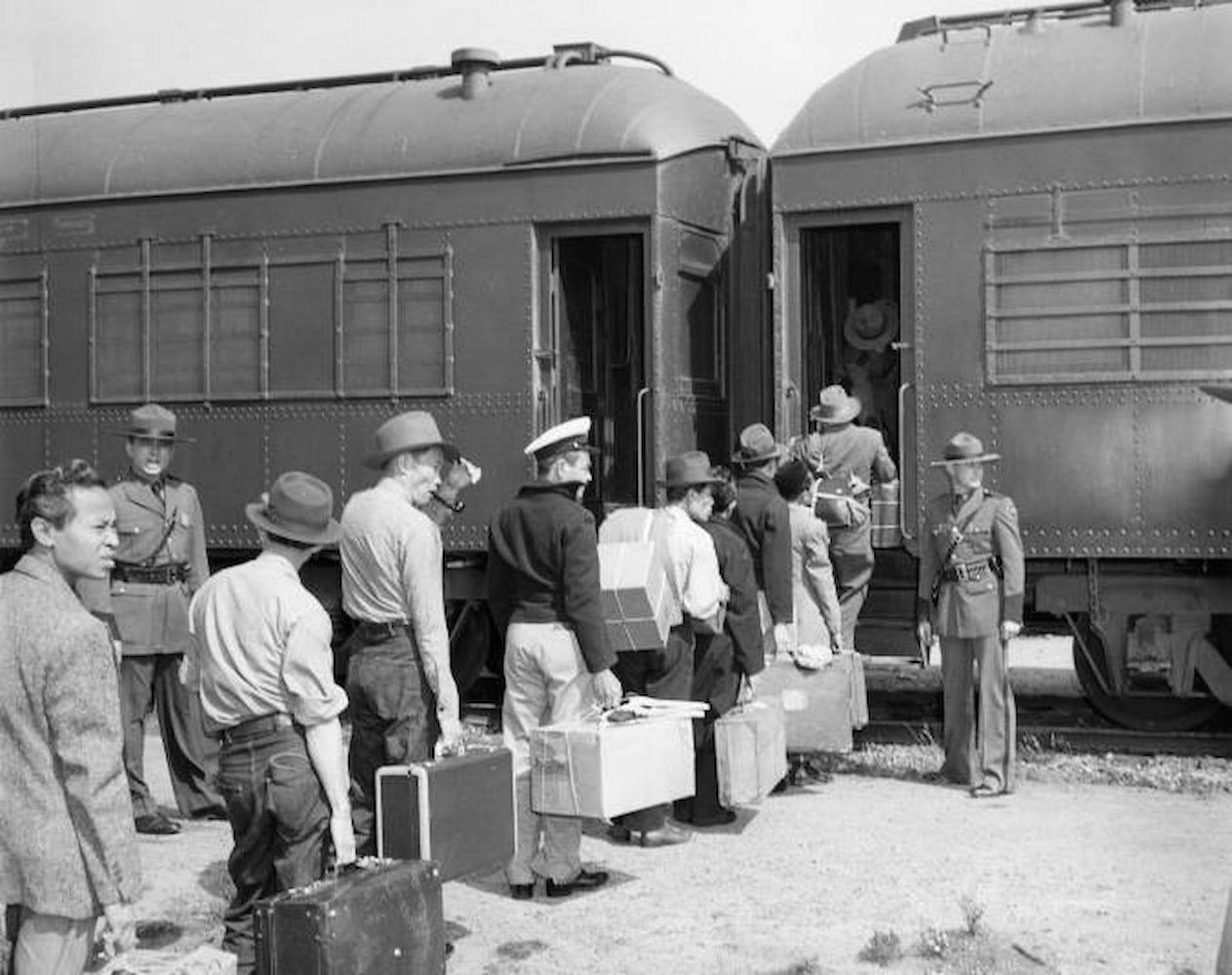 A line of men holding suitcases wait in line to board a train.