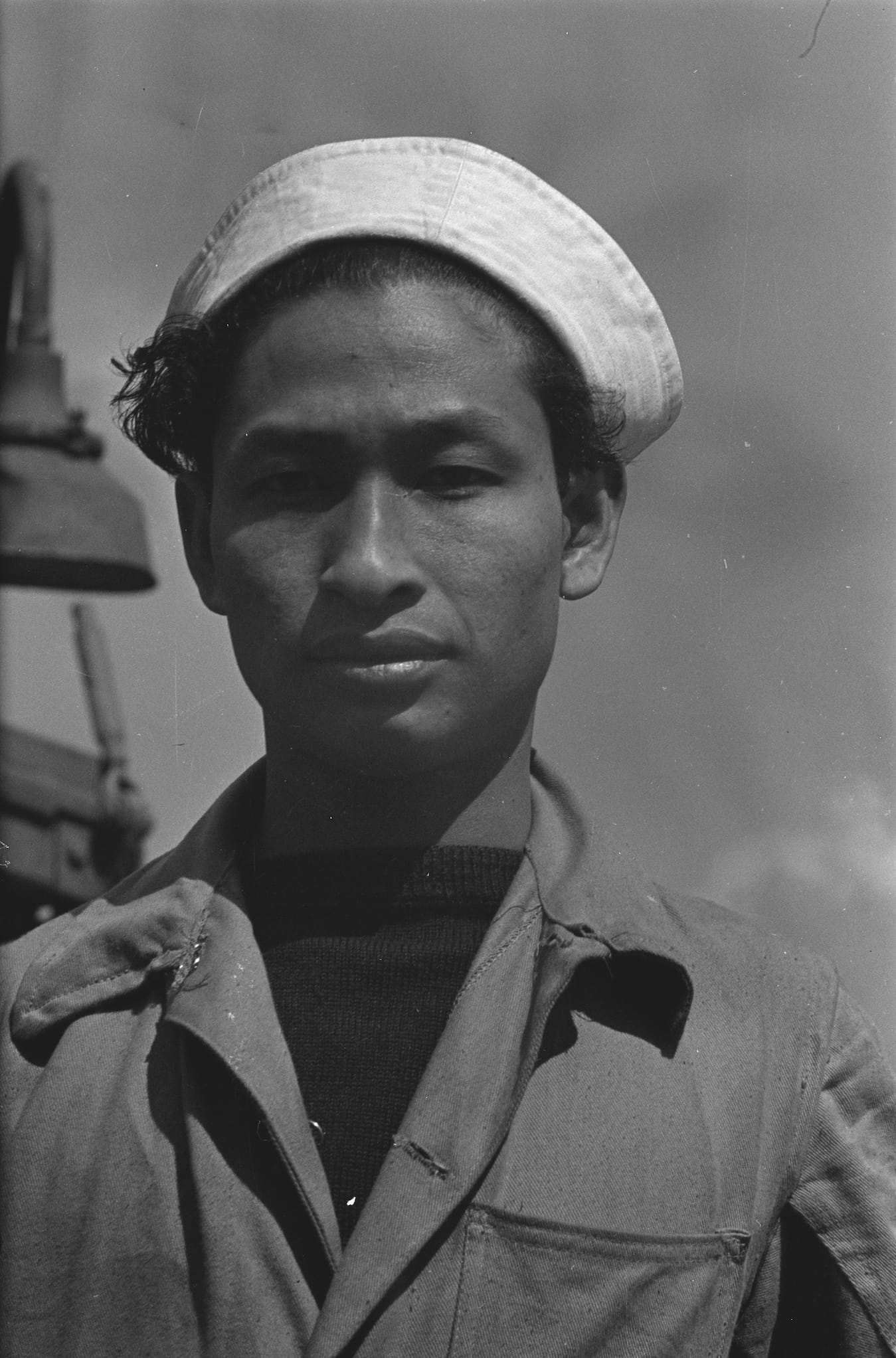 An Indonesian sailor posing in uniform of coveralls and a white hat.