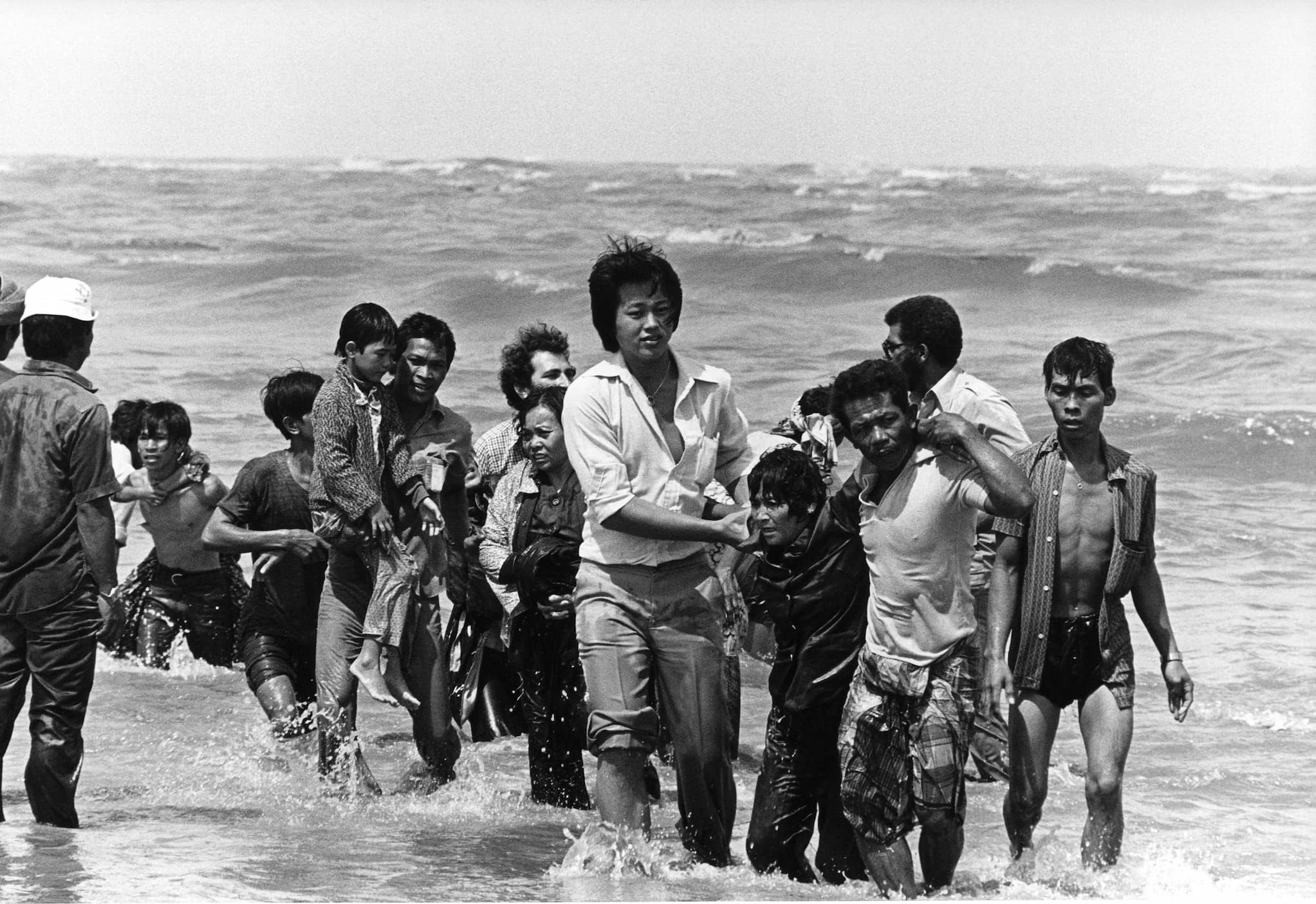 A group of Vietnamese refugees wade through knee deep sea water. They carry no belongings.