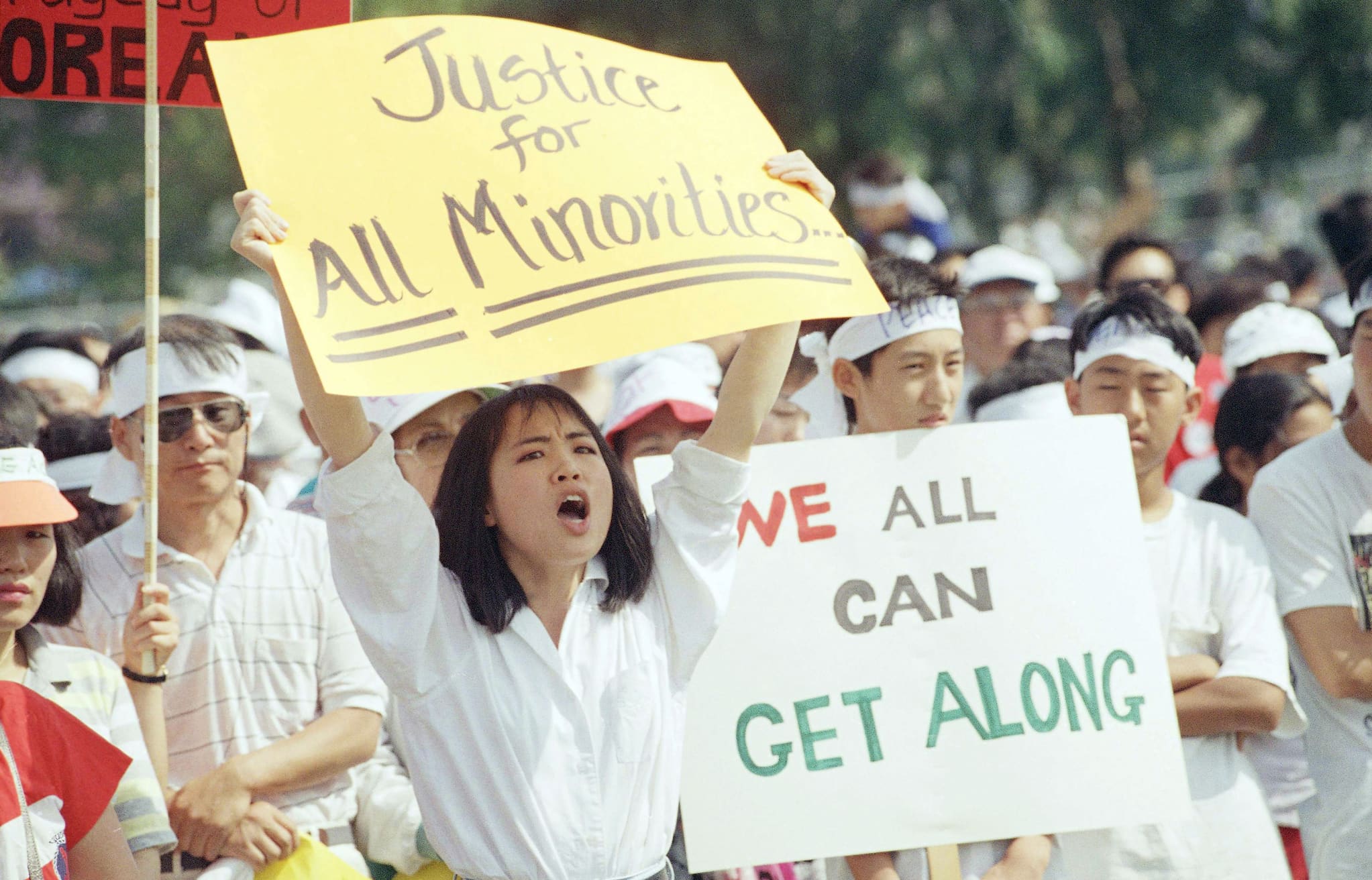 Crowd of people in outdoor gathering. People hold signs calling for healing between the Korean and African American community.
