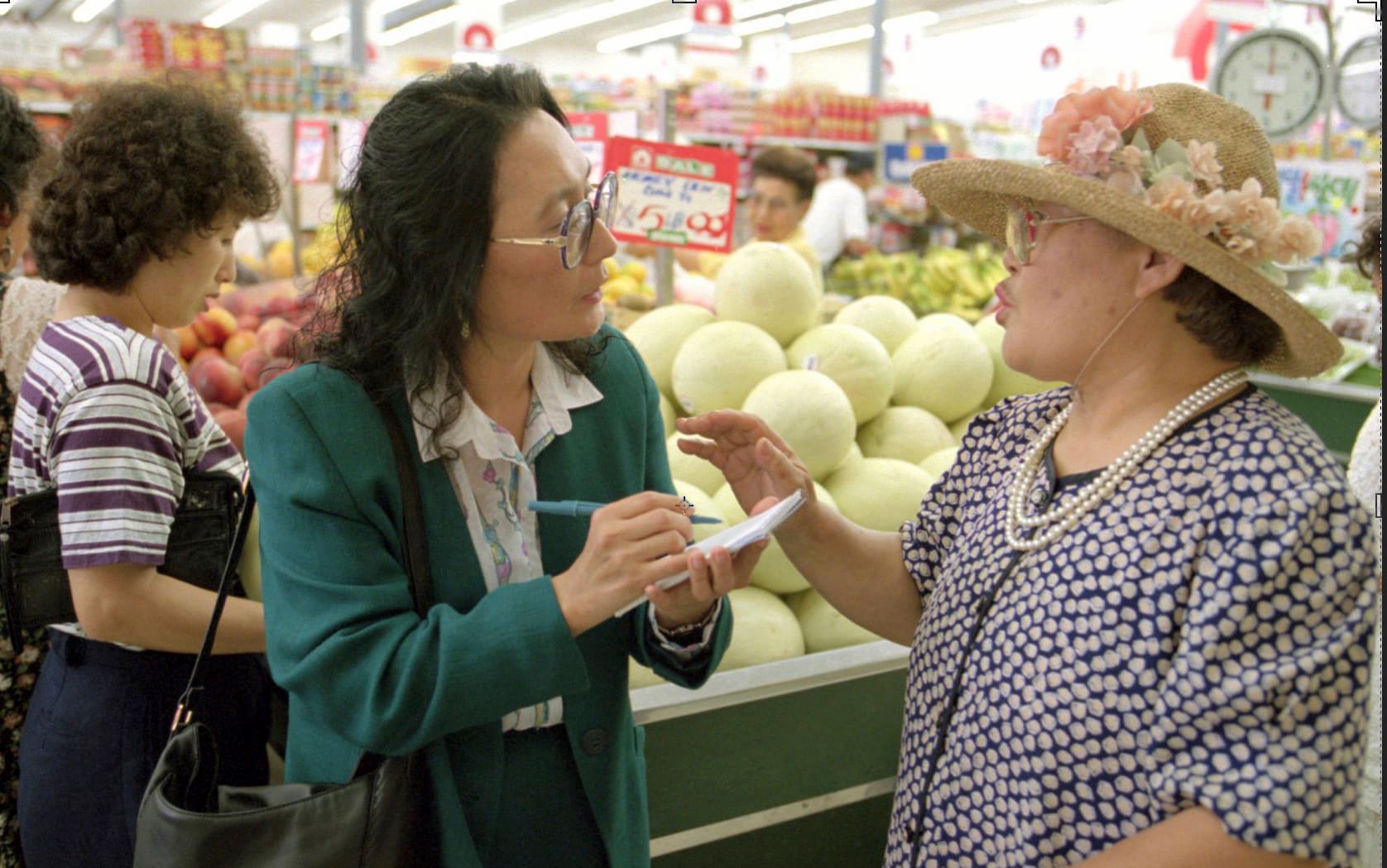 K. Connie Kang, a Korean American journalist, writes on notepad as she interviews woman in supermarket.