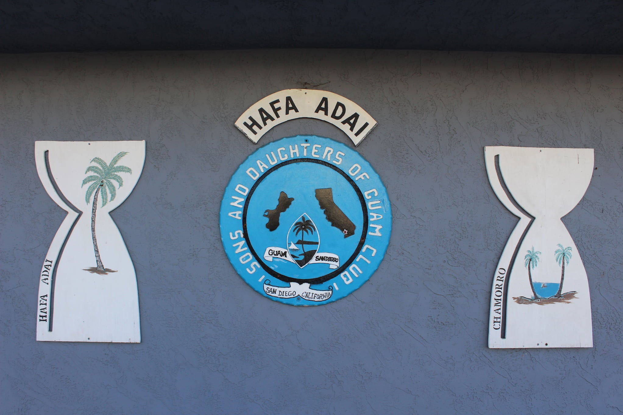 Graphic of circular seal of the Sons and Daughters of Guam Club. Drawings of Guam and California, filled in their respective flags, appear at center.