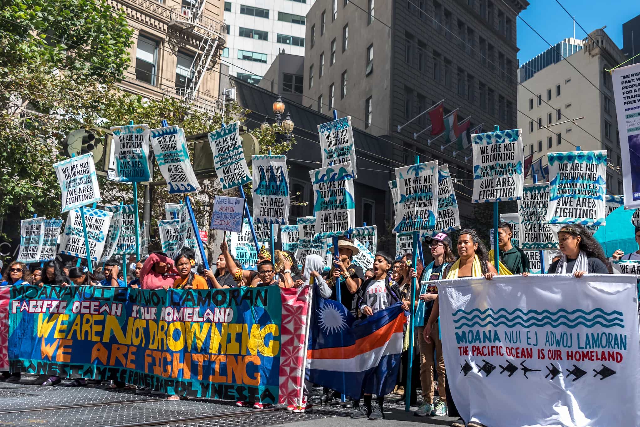 Large group of people stand behind large banners as they gather in street for climate march.