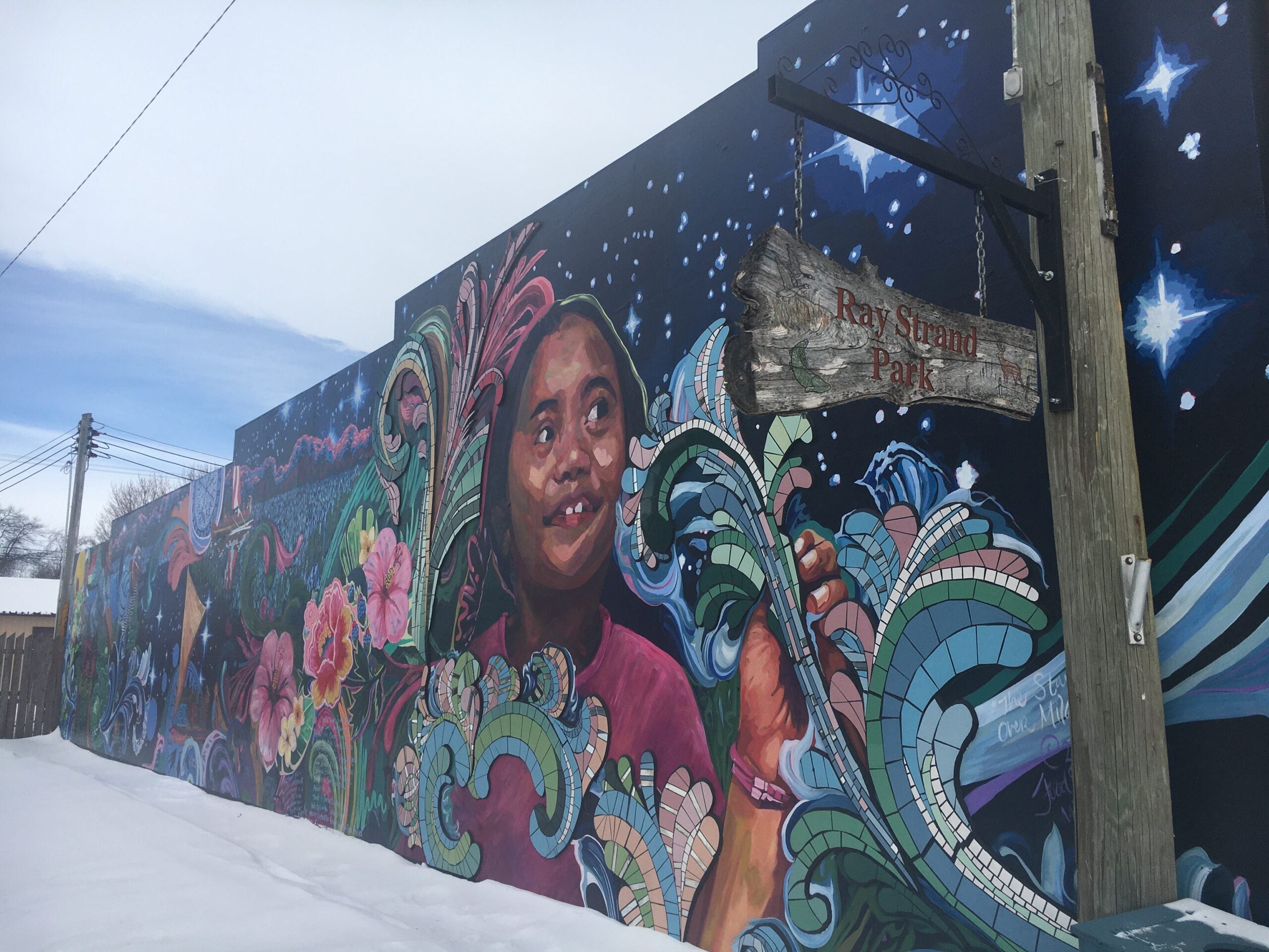 A colorful mural spans the side of a one story building. The mural features a young Micronesian girl surrounded by sprawling flowers and a starry sky.