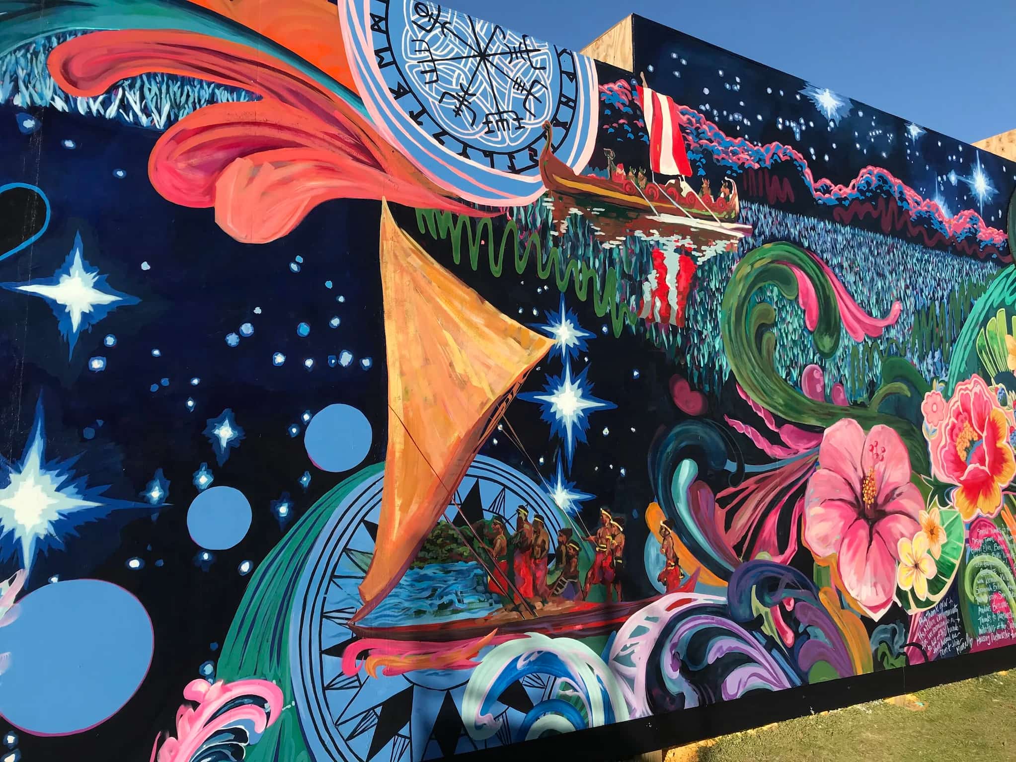 A black, starry night frames a mural with a Polynesian outrigger canoe, over-sized pink flowers and a field of teal and blue reflecting on the water.