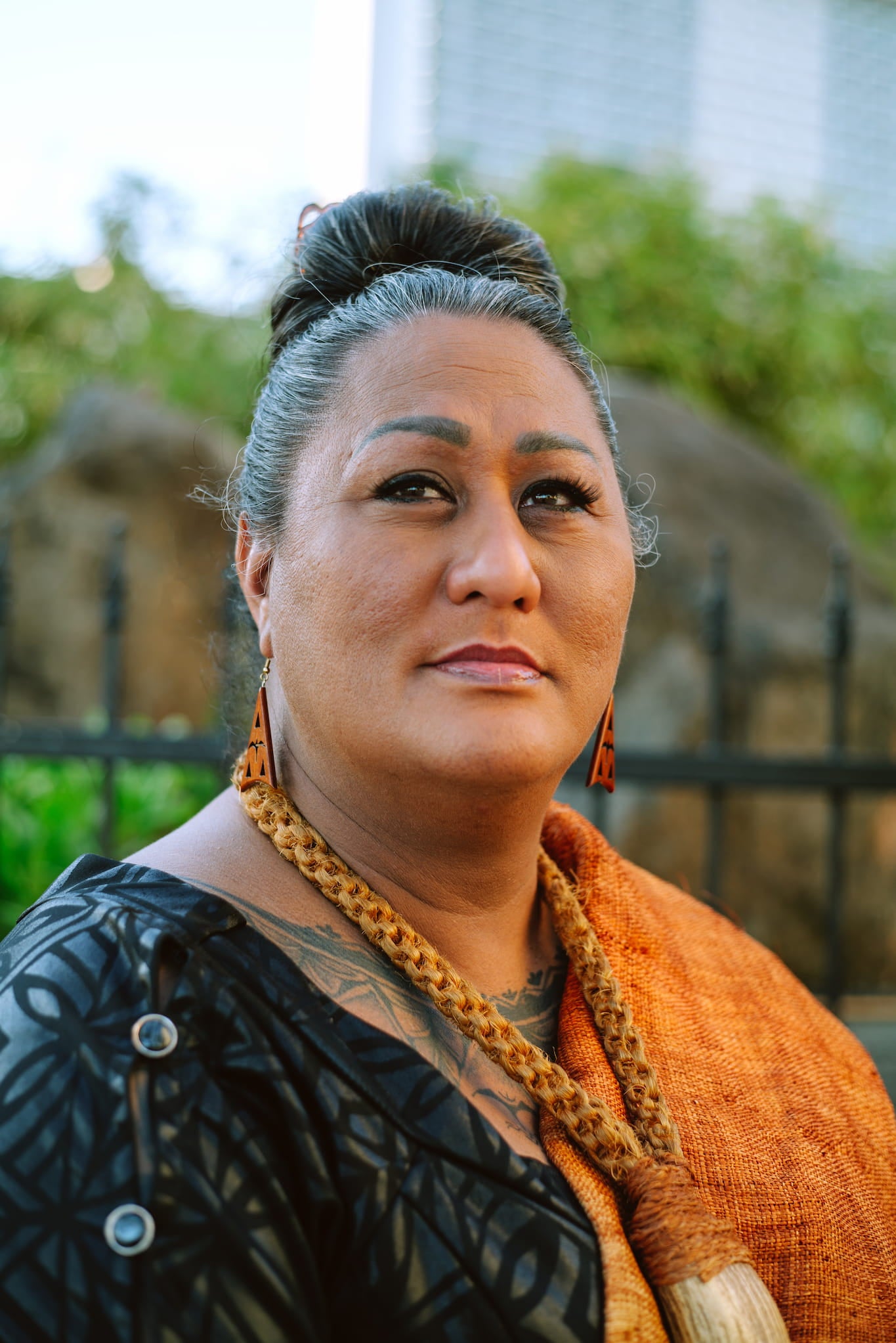 Hina Wong-Kalu, wearing a dress covered by a patterned wrap over her shoulder and a braided lei, poses in outdoor portrait.
