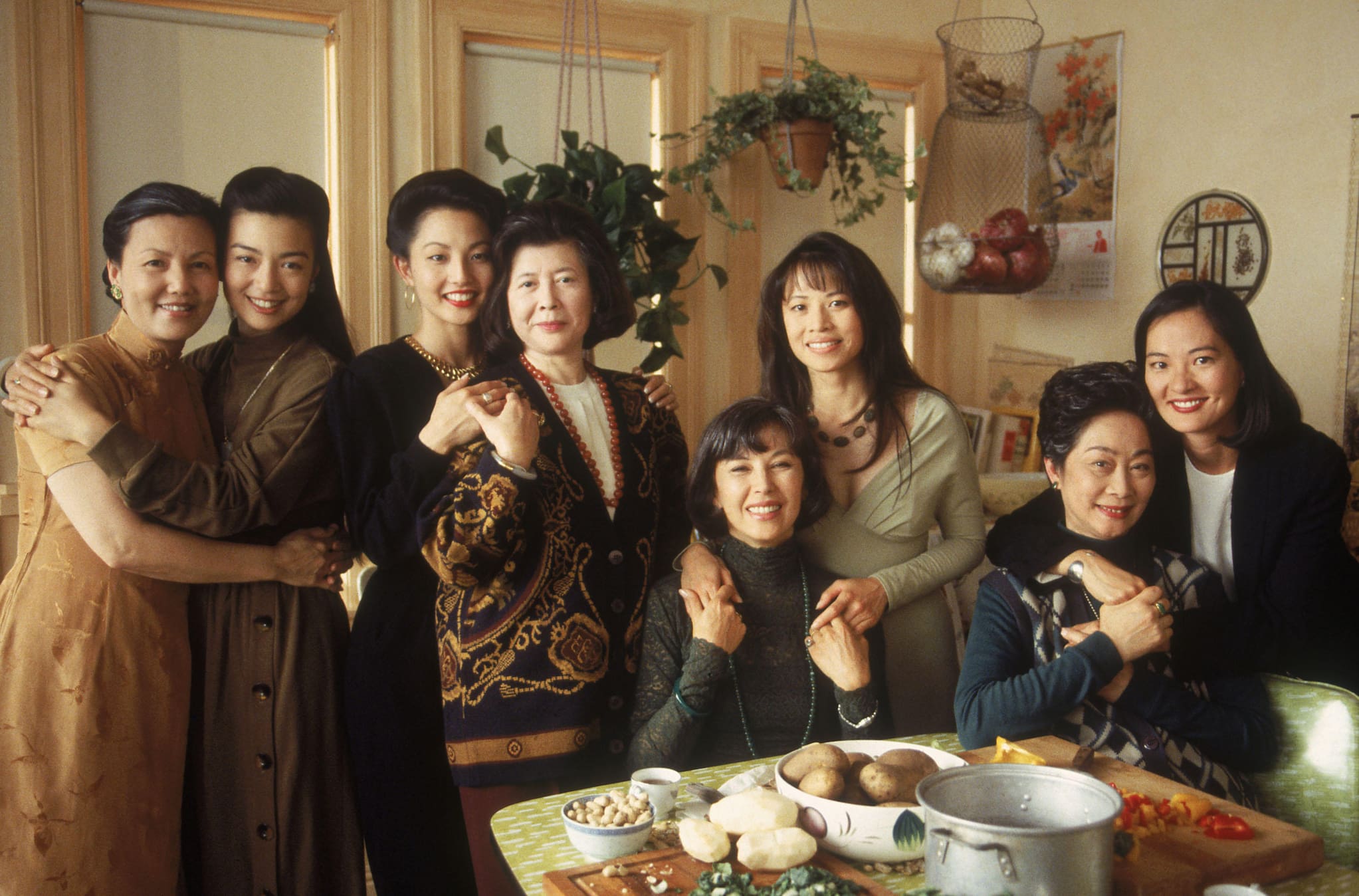 The all-Asian female cast of The Joy Luck Club pose in mother-daughter pairs around dining room table.