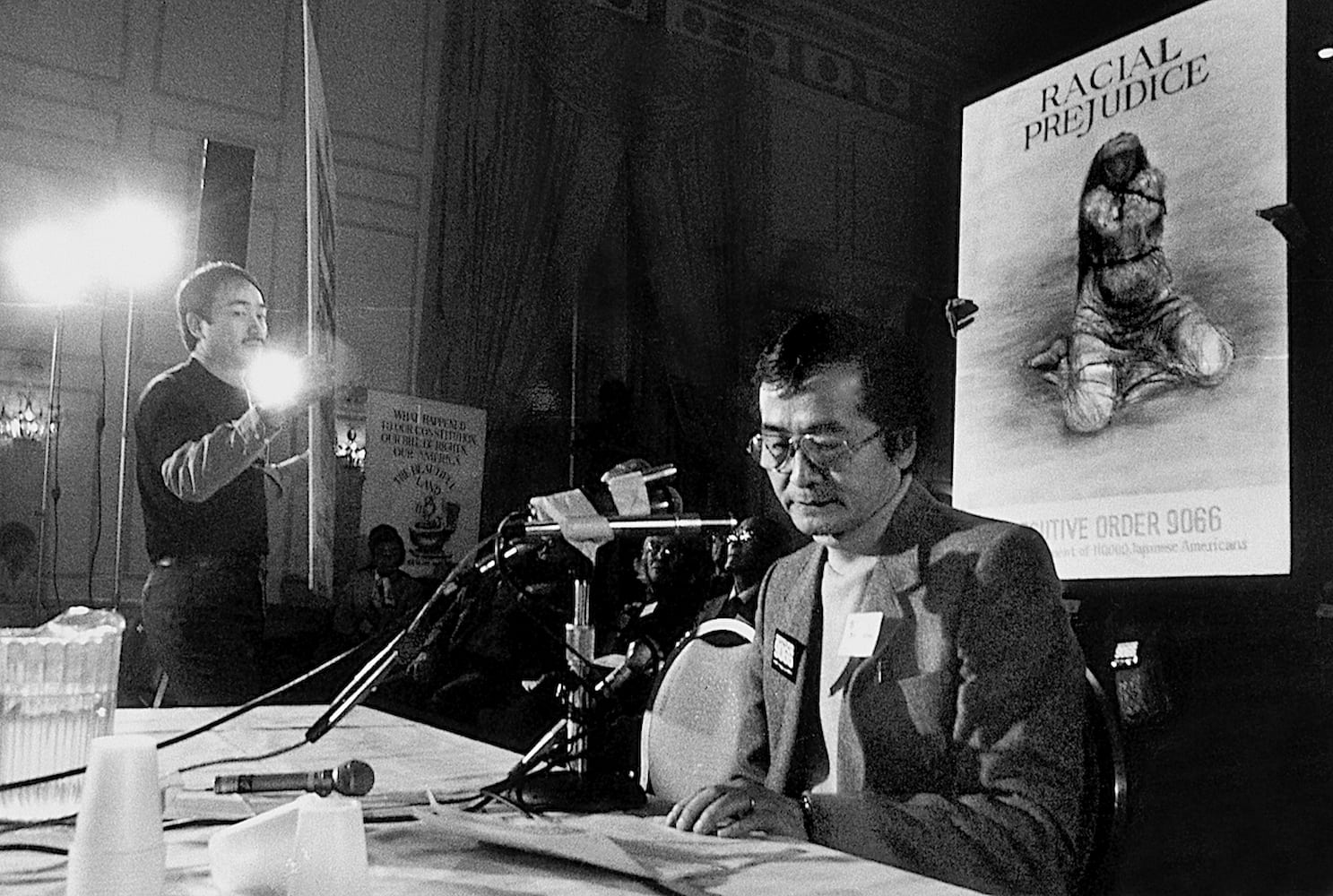Japanese American Bill Kochiyama testifies at the CWRIC hearings. He sits in front of a poster board that reads "Exec. Order 9066 Concentration Camp."