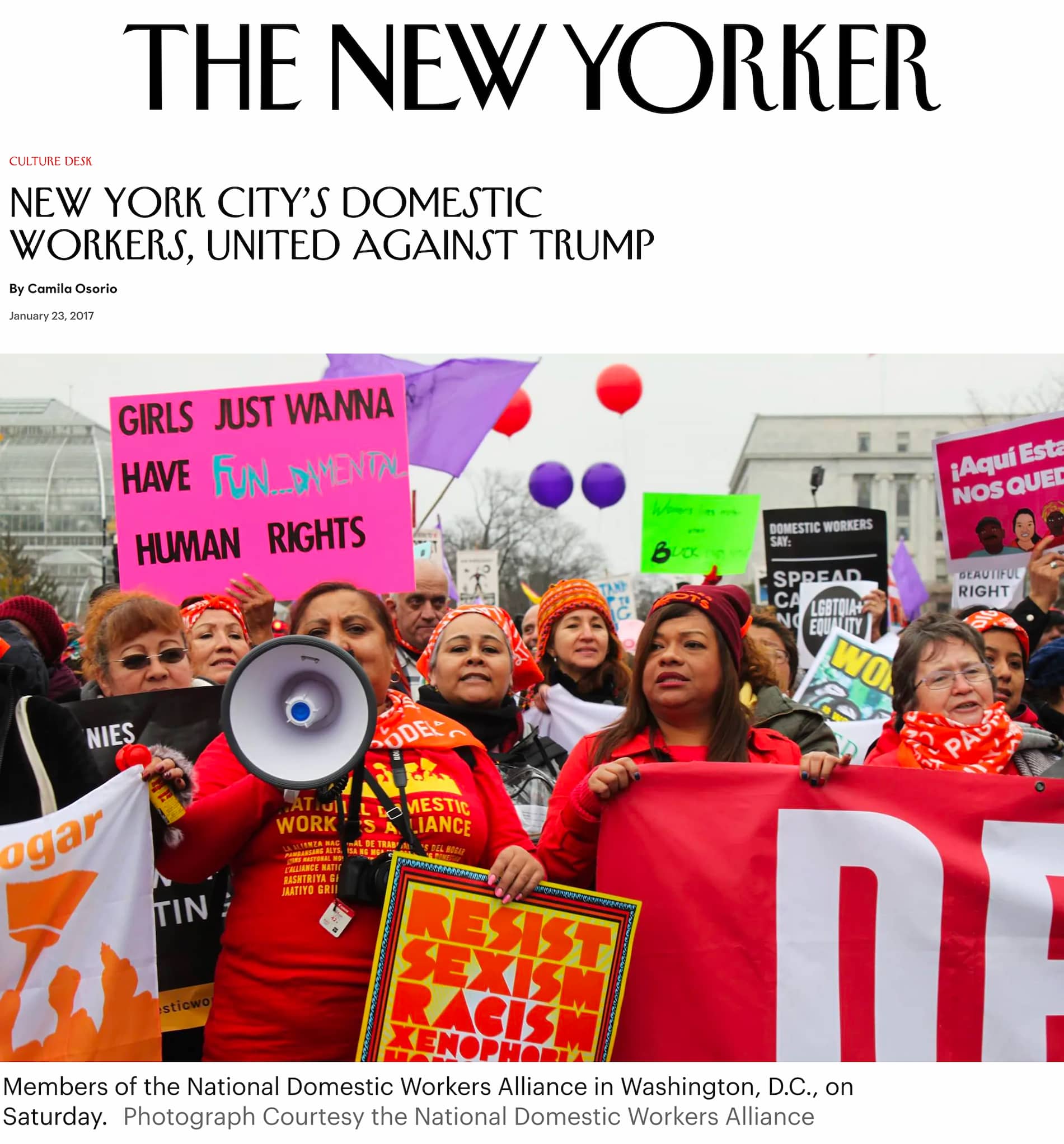 Women of the National Domestic Workers Alliance gather for outdoor march. A woman speaks into a megaphone and others hold up signs.