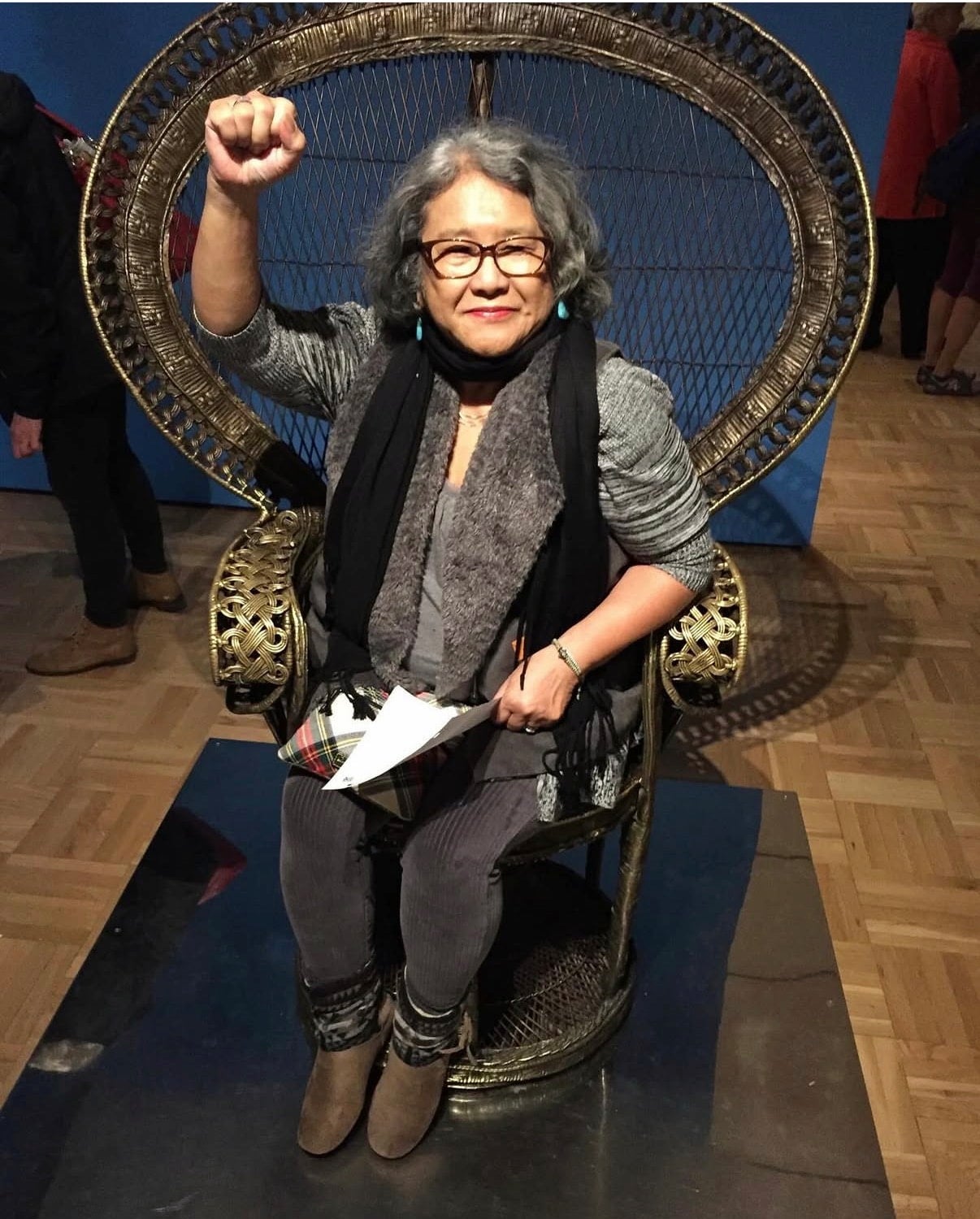 Estella Habal sitting in an ornate highback chair smiling and holding one fist above her head.