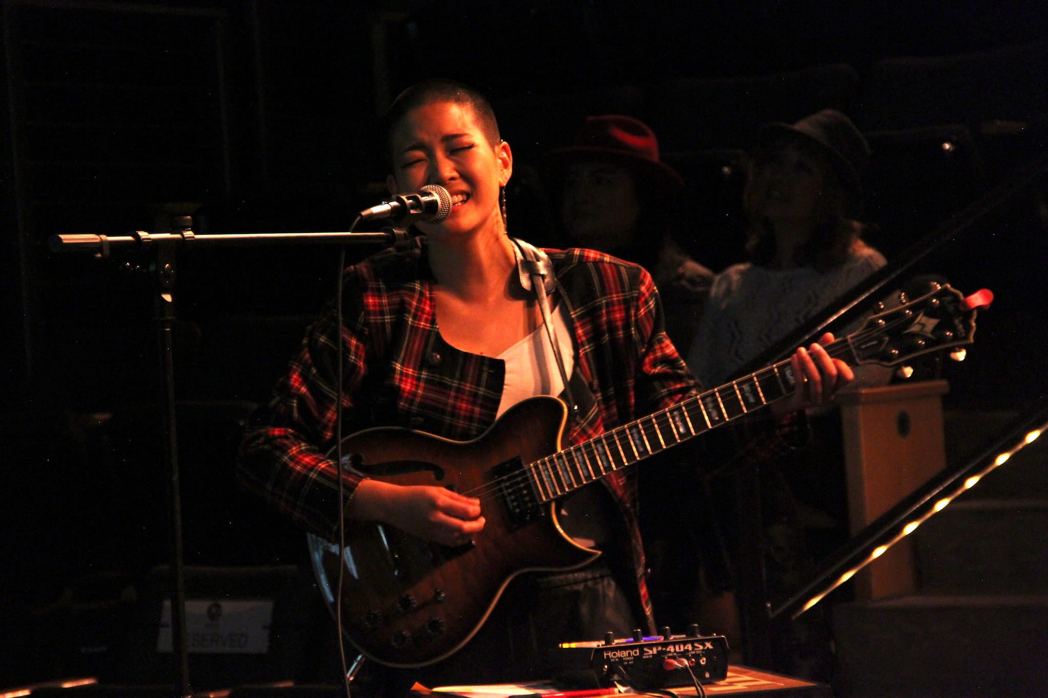 Kyoko Takenaka holding a guitar and signing into a microphone.