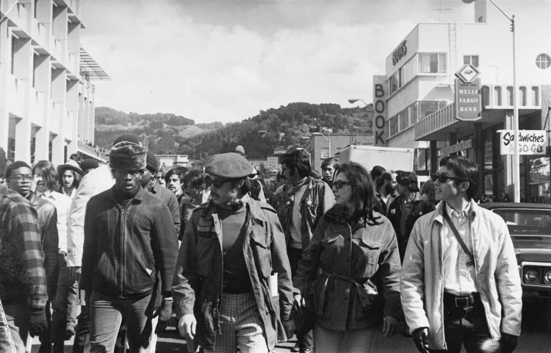 Four student leaders of the Third World Liberation Front march down a UC Berkeley street. A crowd marches behind them.