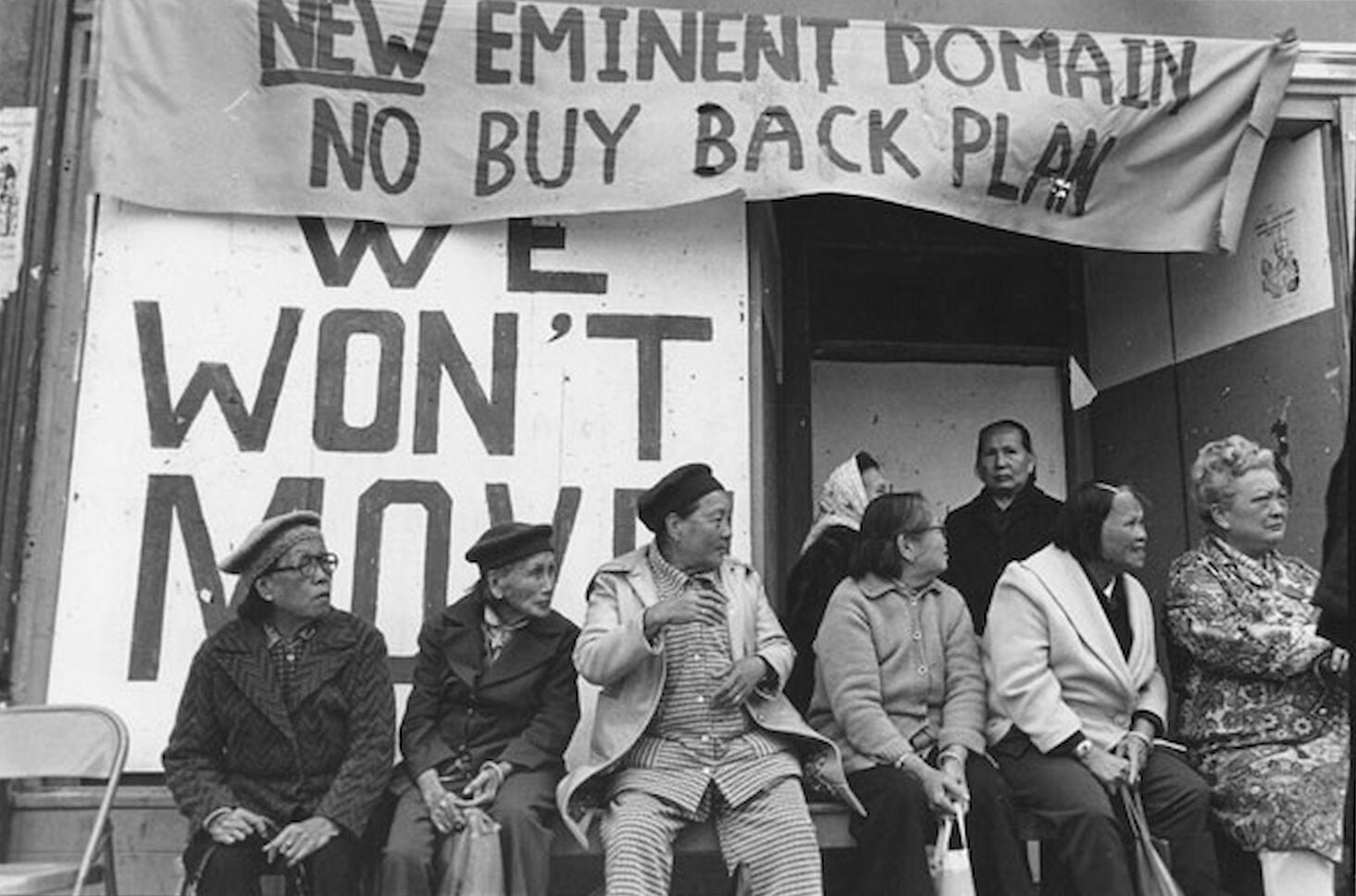 People protesting I-Hotel eviction sit and stand outside of the building. They gather in front of a large sign with the words "We Won't Move."
