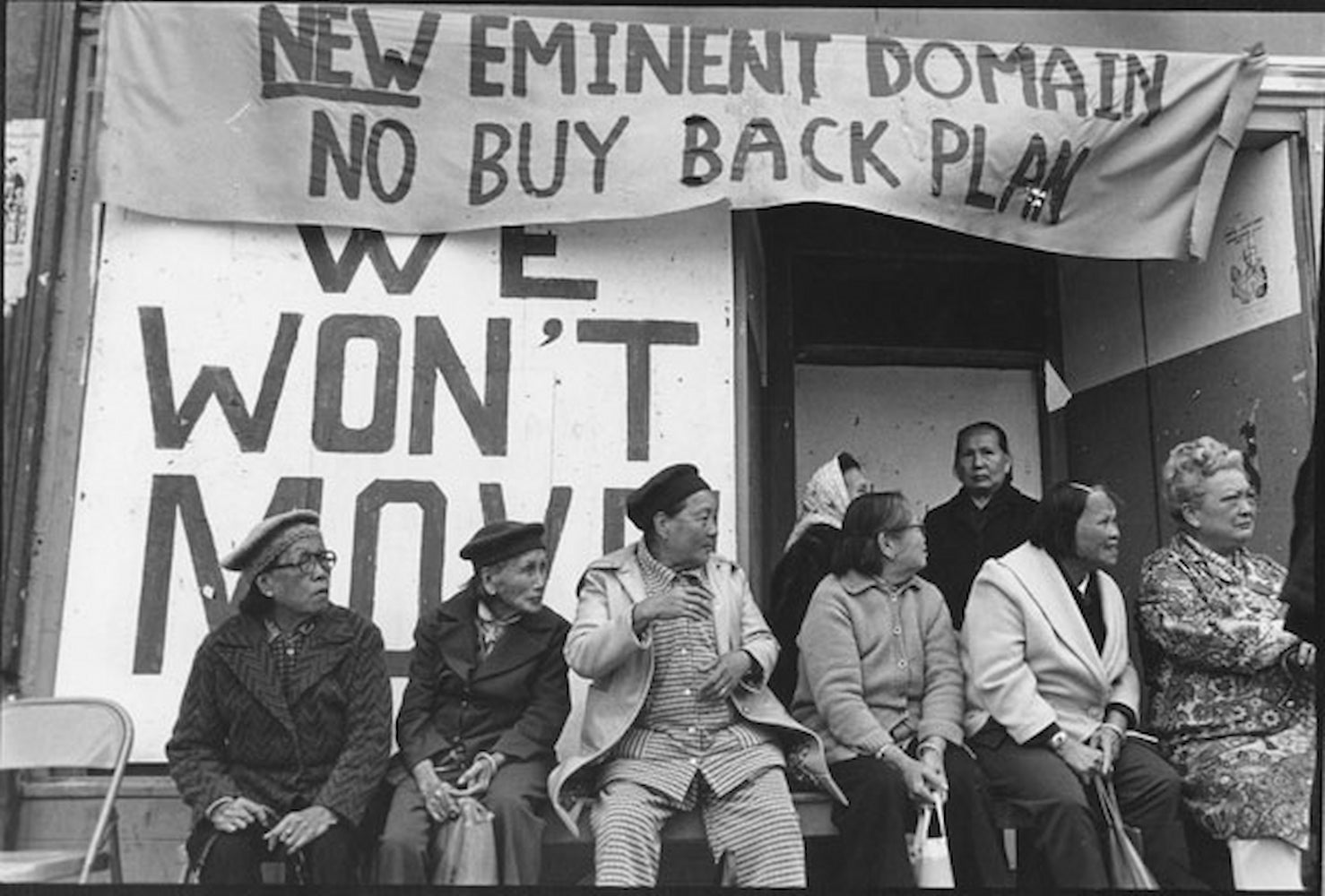 People protesting I-Hotel eviction sit and stand outside of the building. They gather in front of a large sign with the words "We Won't Move."