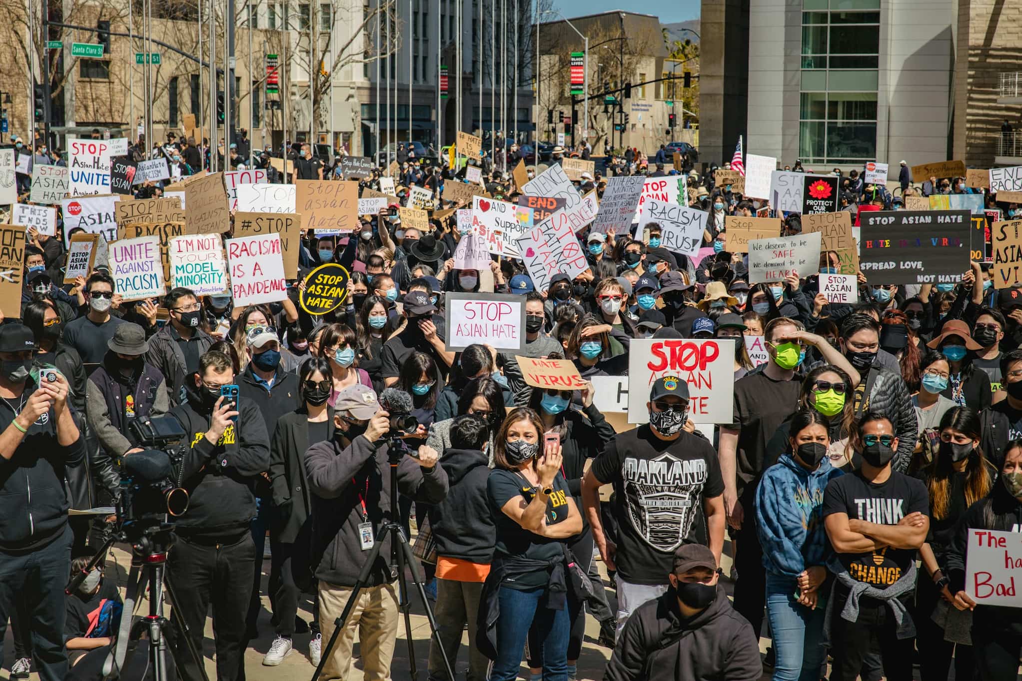 Protestors wearing masks and holding various signs while facing towards the camera at a StopAsianHate community rally in San Jose.