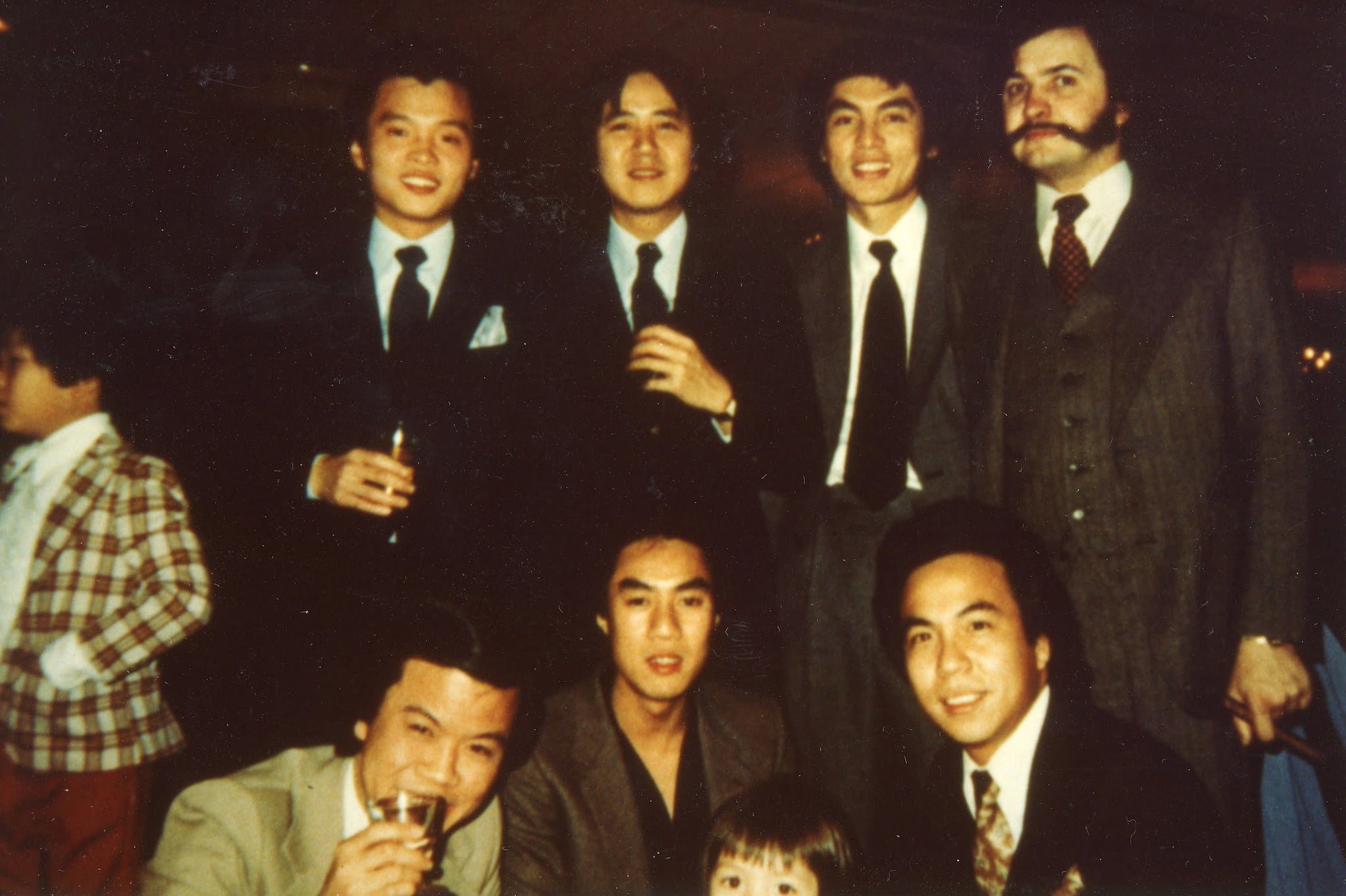 Vincent Chin, a Chinese American man wearing a printed tie and black suit jacket, crouches in front row of group photo with similarly dressed friends.