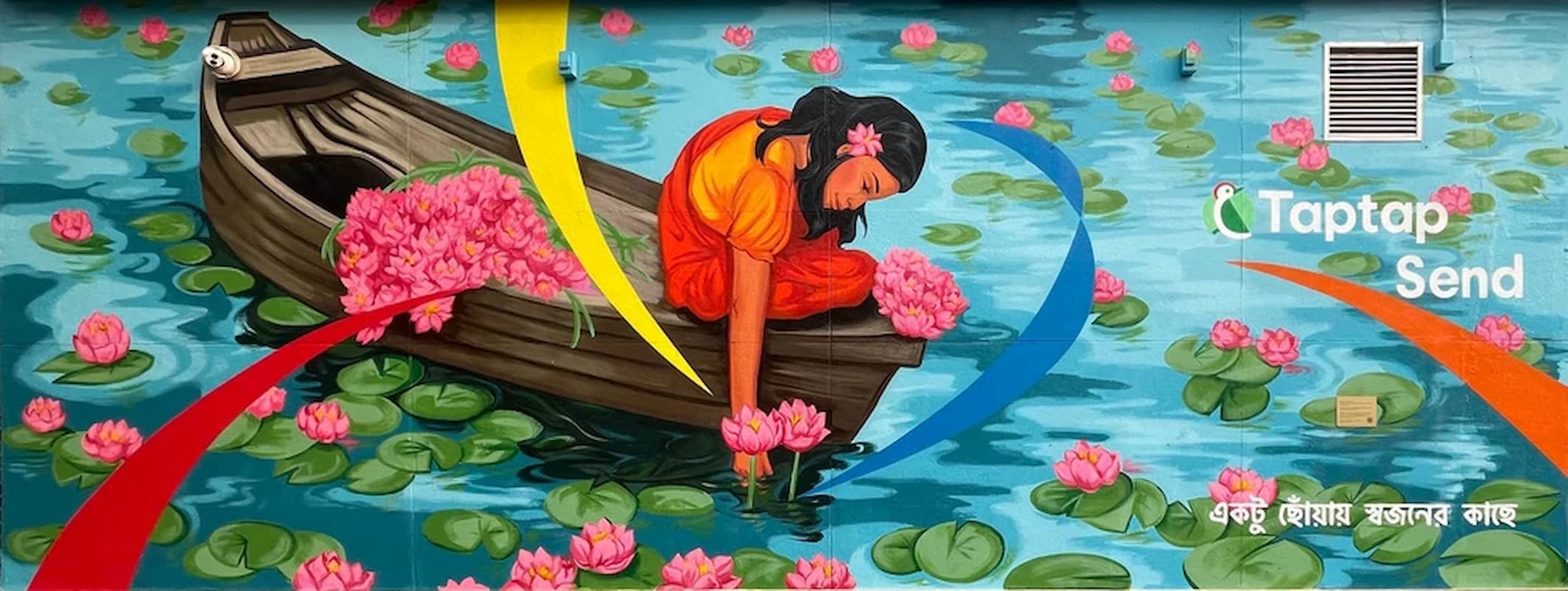 Mural depicts a young girl wearing a saree on a boat floating in the water amongst lily pads as she handpicks another shapla for her collection.