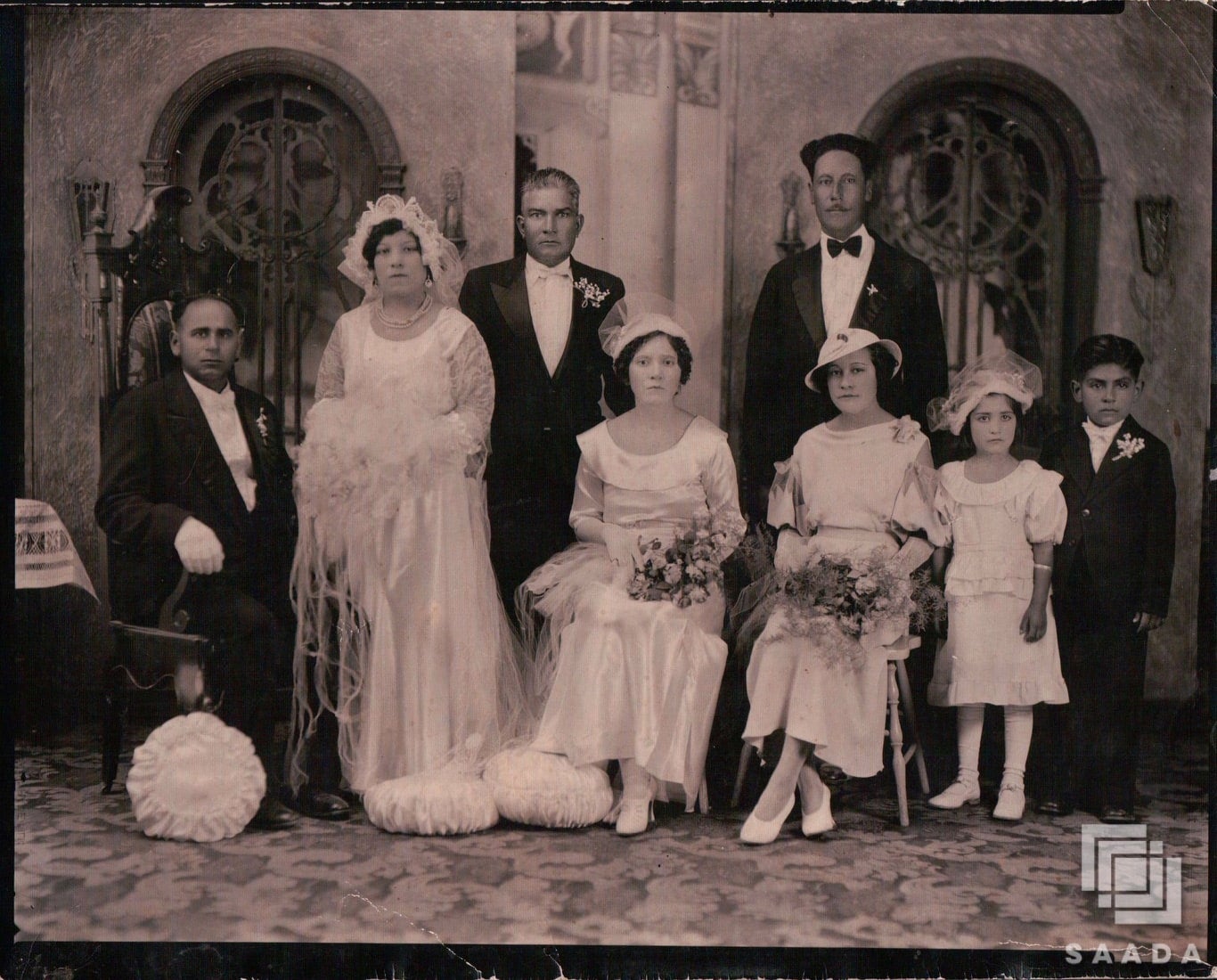 Punjabi Mexican wedding family photo. Three women and young girl wear white dresses with bonnets while three men and young boy wear black suits.