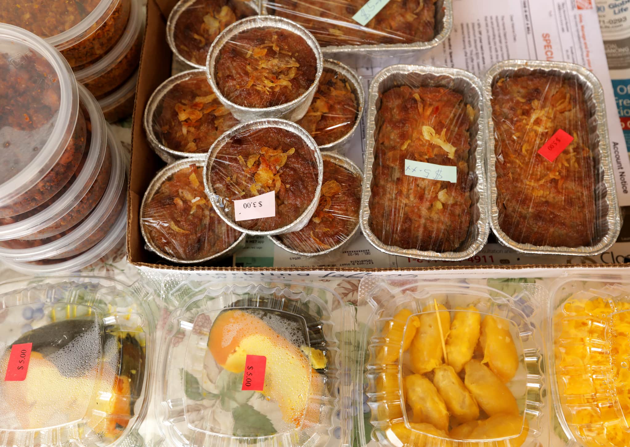 Overhead shot of Thai dishes prepared and wrapped in aluminum ramekins and plastic to-go containers, atop table at outdoor market.