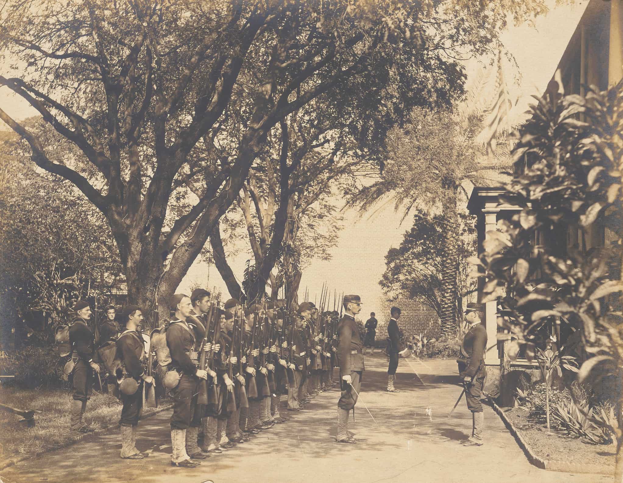 U.S. Marines in uniform stand at attention with their rifles outside of ʻIolani Palace. Three officers stand at attention with their swords.