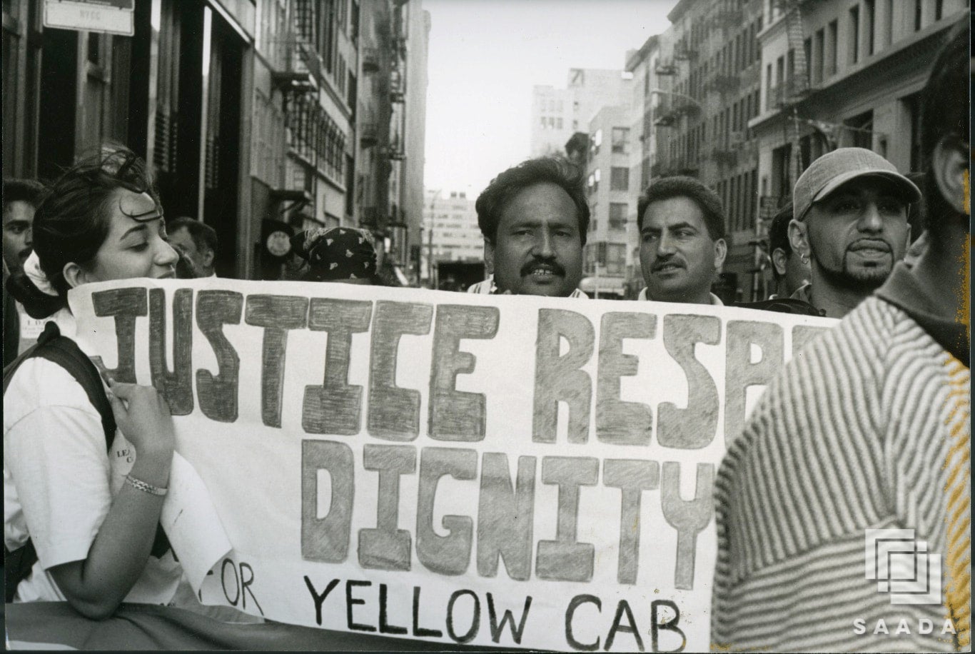 Lease Drivers Coalition members gather in street for protest. Several people stand behind banner reading "Justice. Respect. Dignity."