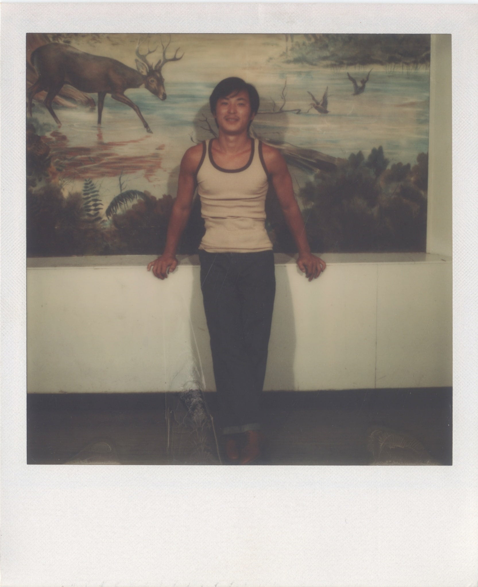 Chol Soo Lee in a tank top smiling in front of a painted mural. The mural shows an elk in a river.