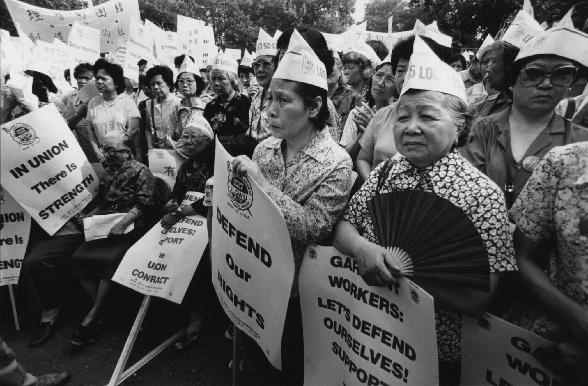 A group of women sitting and standing wear "Local 23-25" hats and hold pro-union picket signs. The group looks off camera-left.
