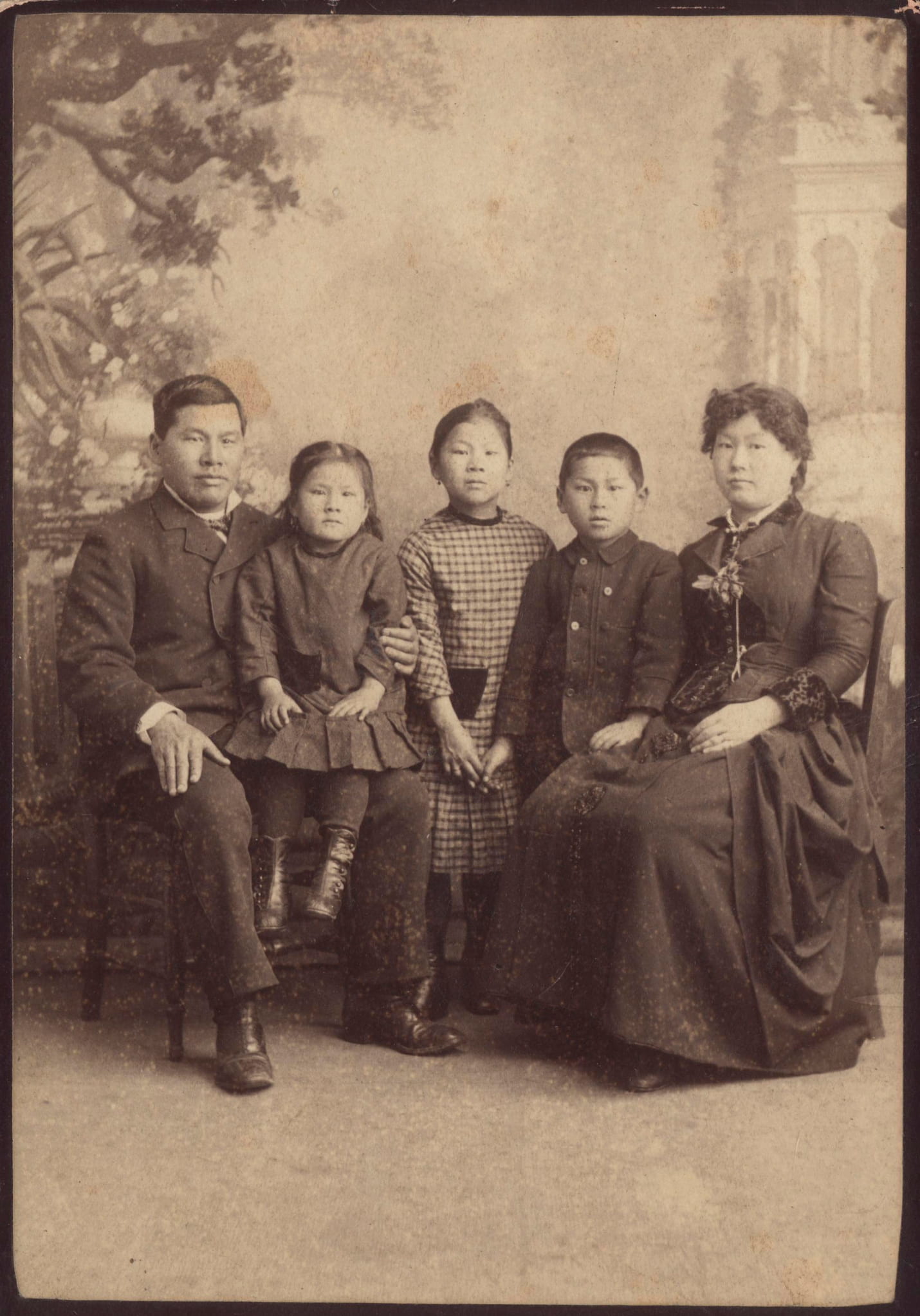 A formally dressed Tape family poses for a portrait. The parents sit at each end with the children in the center.