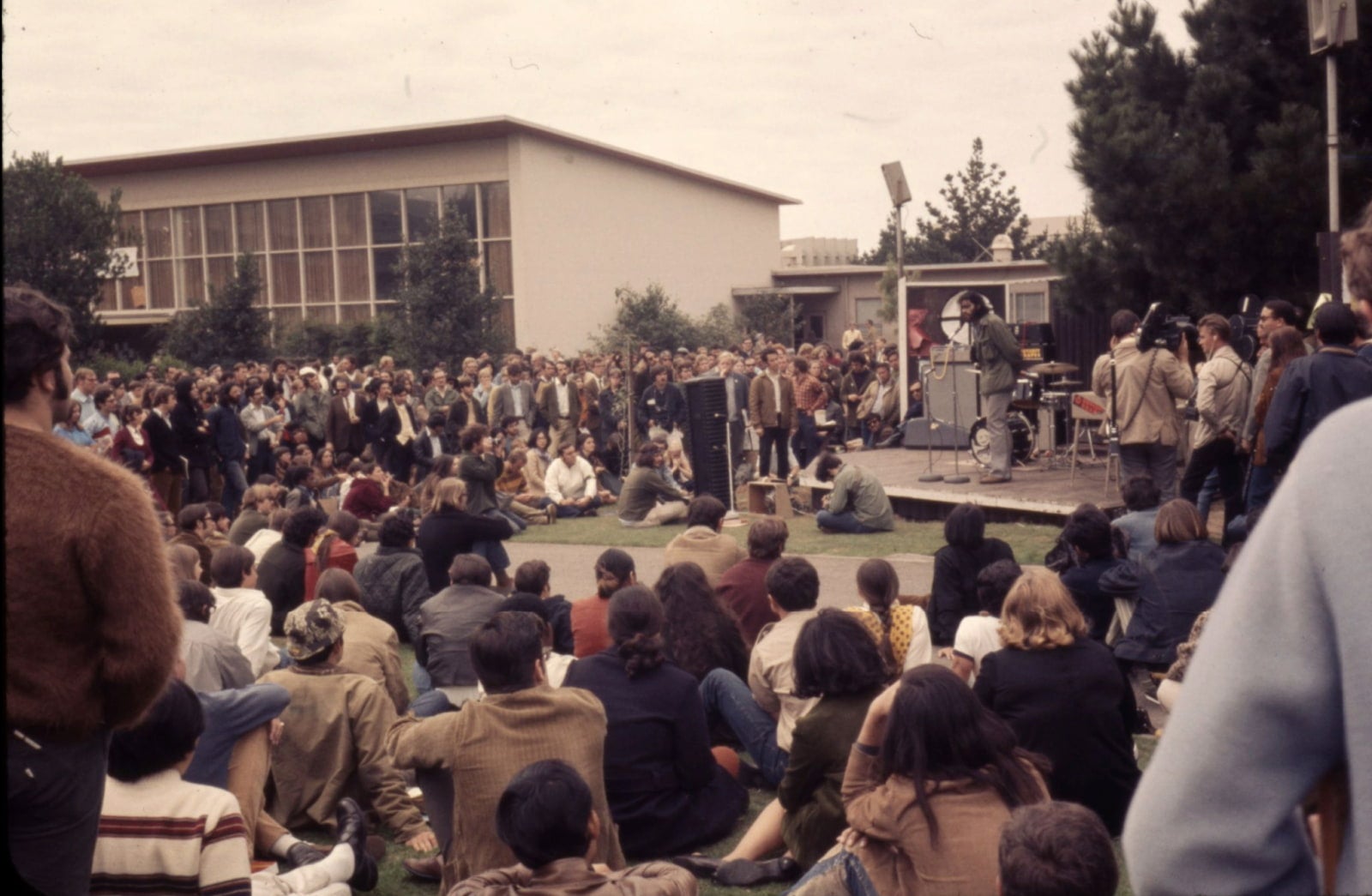 A large crowd gathers in the commons to listen to Roger Alvarado. Reporters film the scene.