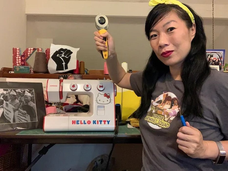 Kristina Wong wears an Auntie Sewing Squad shirt. Her sewing room has a Hello Kitty sewing machine, bobbins, photos and a scrap of a closed fist.