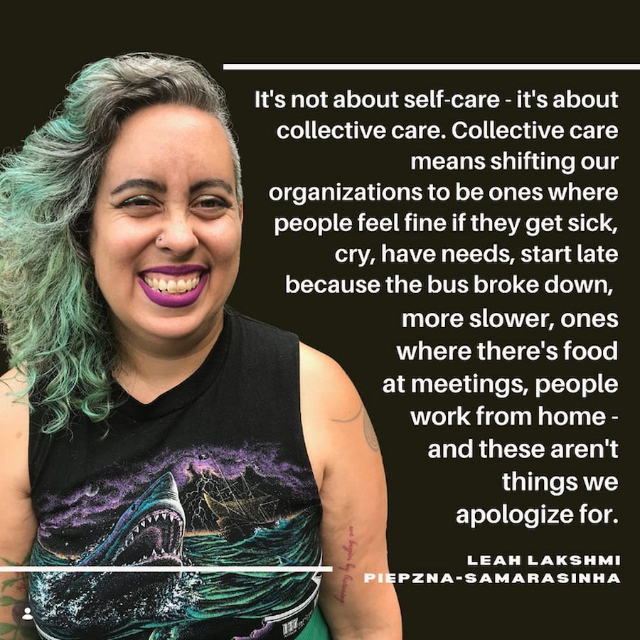 A woman with a big smile wears green hair, purple lipstick, and a sleeveless, black t-shirt with a graphic of a shark in a storm.