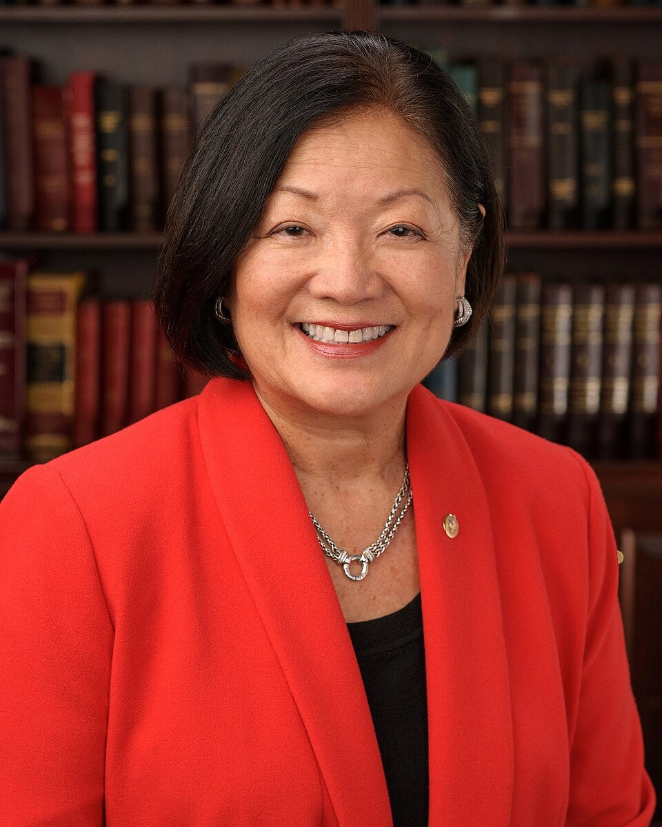 Formal portrait of Mazie Hirono with rows of books as a background.