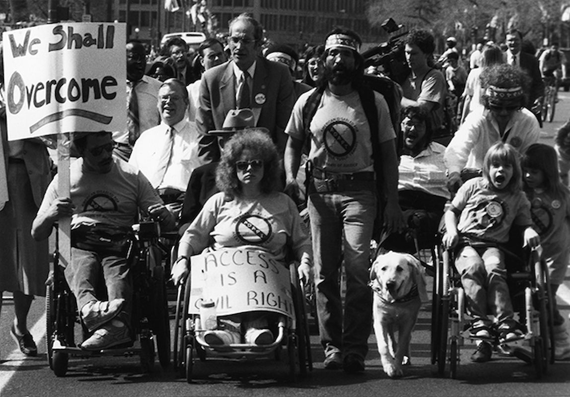 The front line of a protest has people in wheelchairs and a service dog.