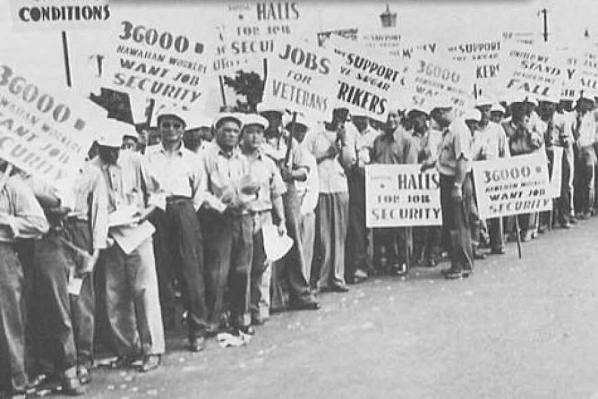 A row of men wearing button-down shirts, long pants and caps hold signs striking for job security and support for veterans.