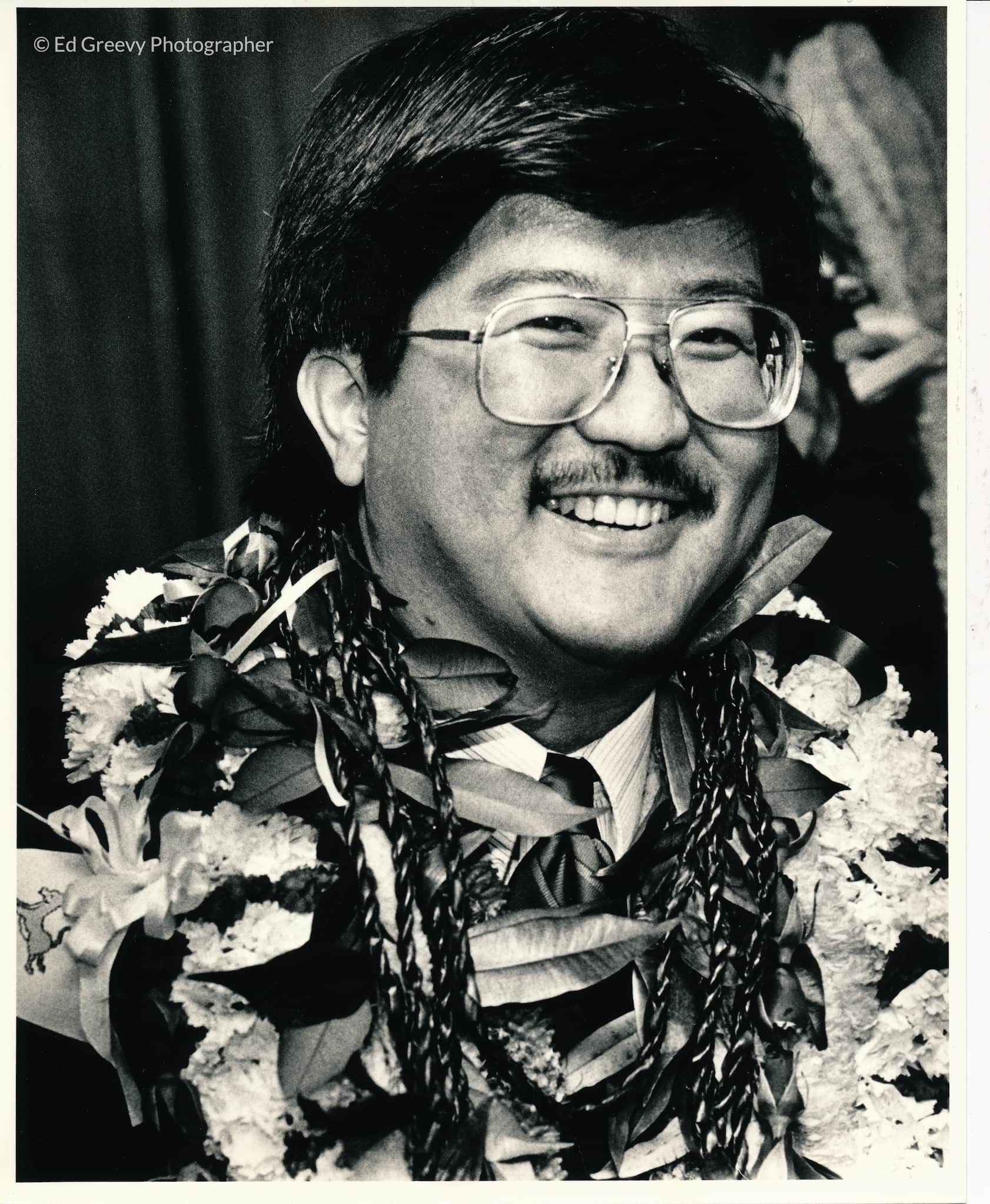 Roland Kotani wears a large smile and several floral and leafy leis.