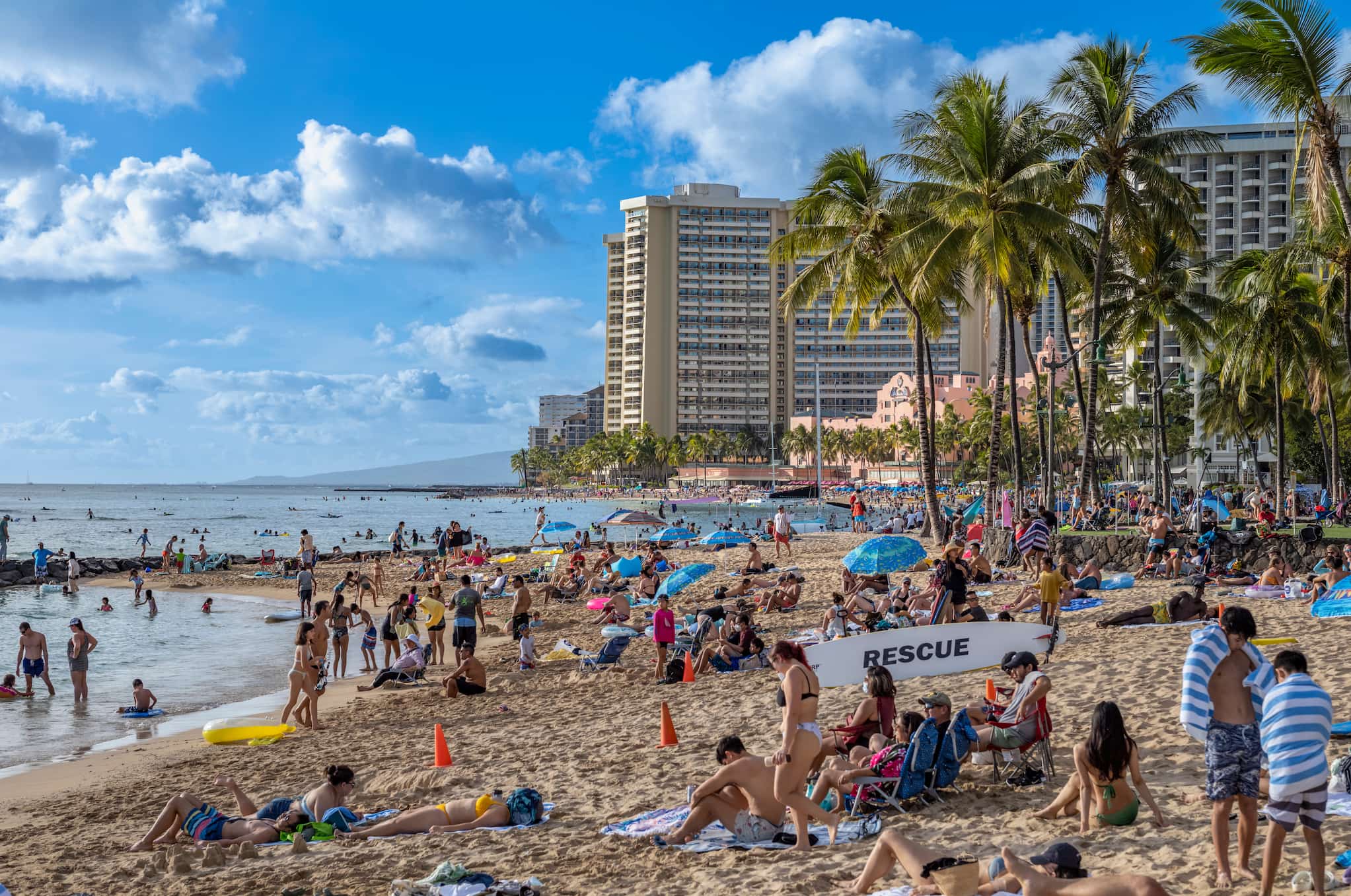 A beach and ocean front packed with people. Hotels dominate the background.