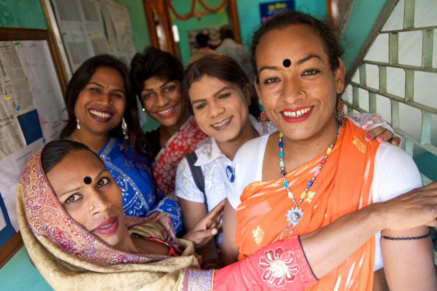 A group of Hijra, all smiling, pose together in a hallway.