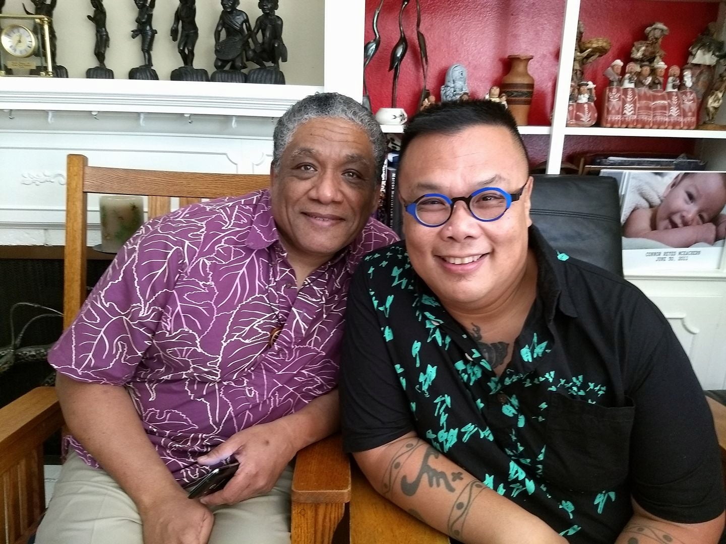 Ric Parish and Joël Barraquiel Tan lean in towards one another smiling for a photo. Several pictures are seen in the background.