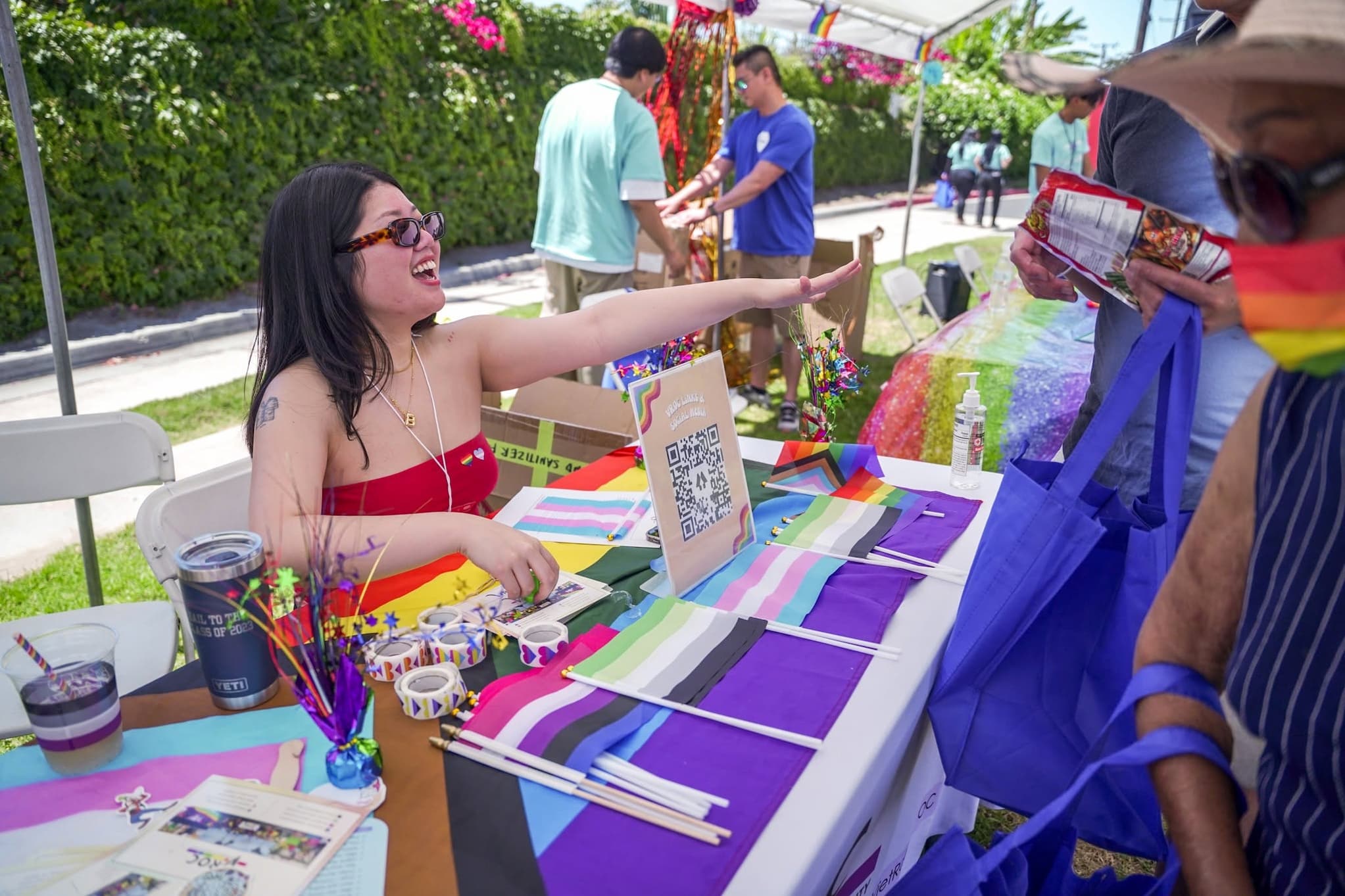 An outdoor covered table along a sidewalk displays stickers and flags with different colored stripes.