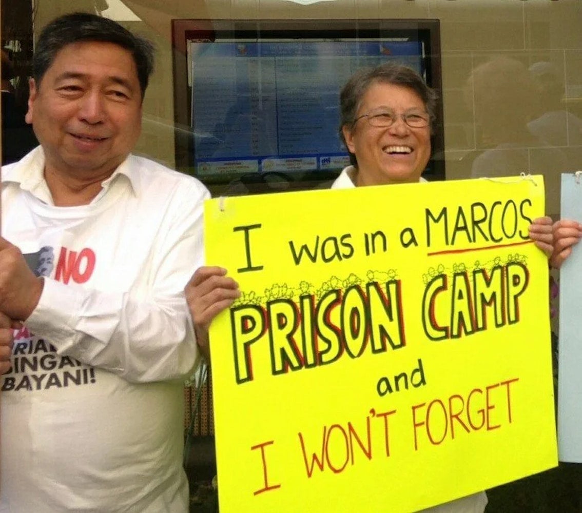 Although posing with a smile, Melinda Paras holds a sign about being held in a prison camp.