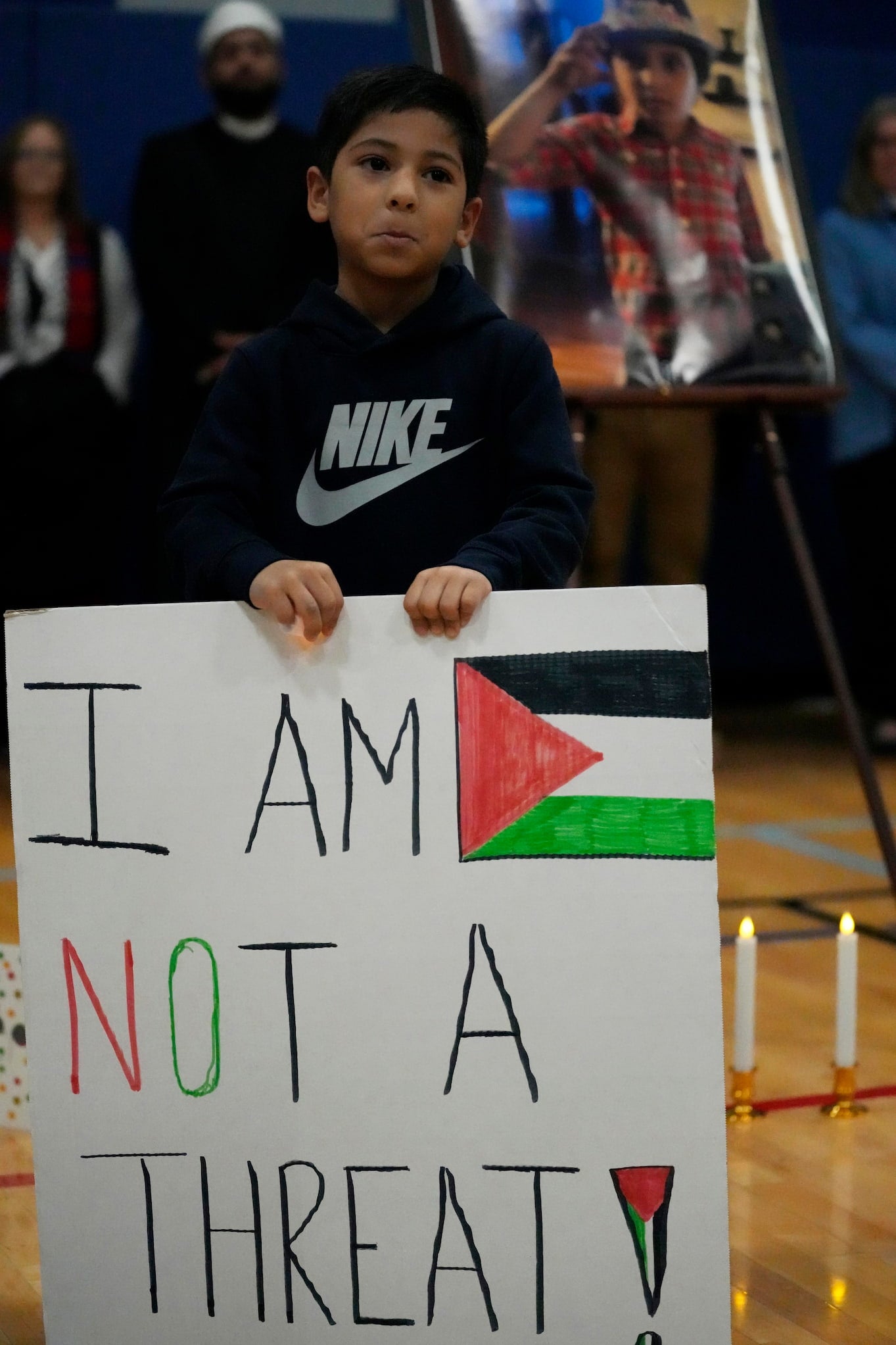 At indoor vigil for Wadee Alfayoumi, a young Palestinian American boy stands behind a sign that reads, "I Am Not A Threat."