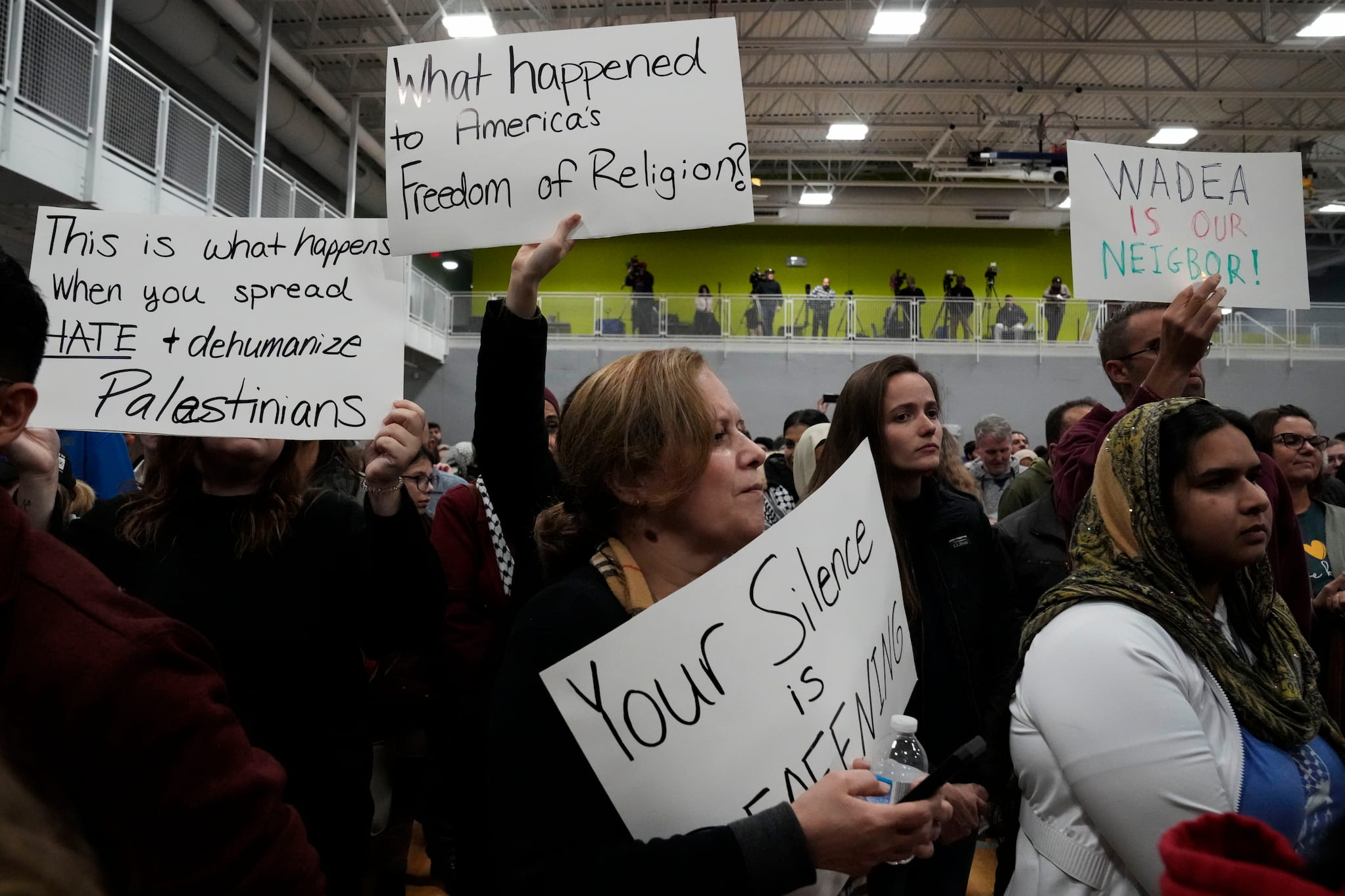 Community members gathered inside a recreation center in Plainfield, Illinois hold up signs during a vigil for Wadee Alfayoumi.