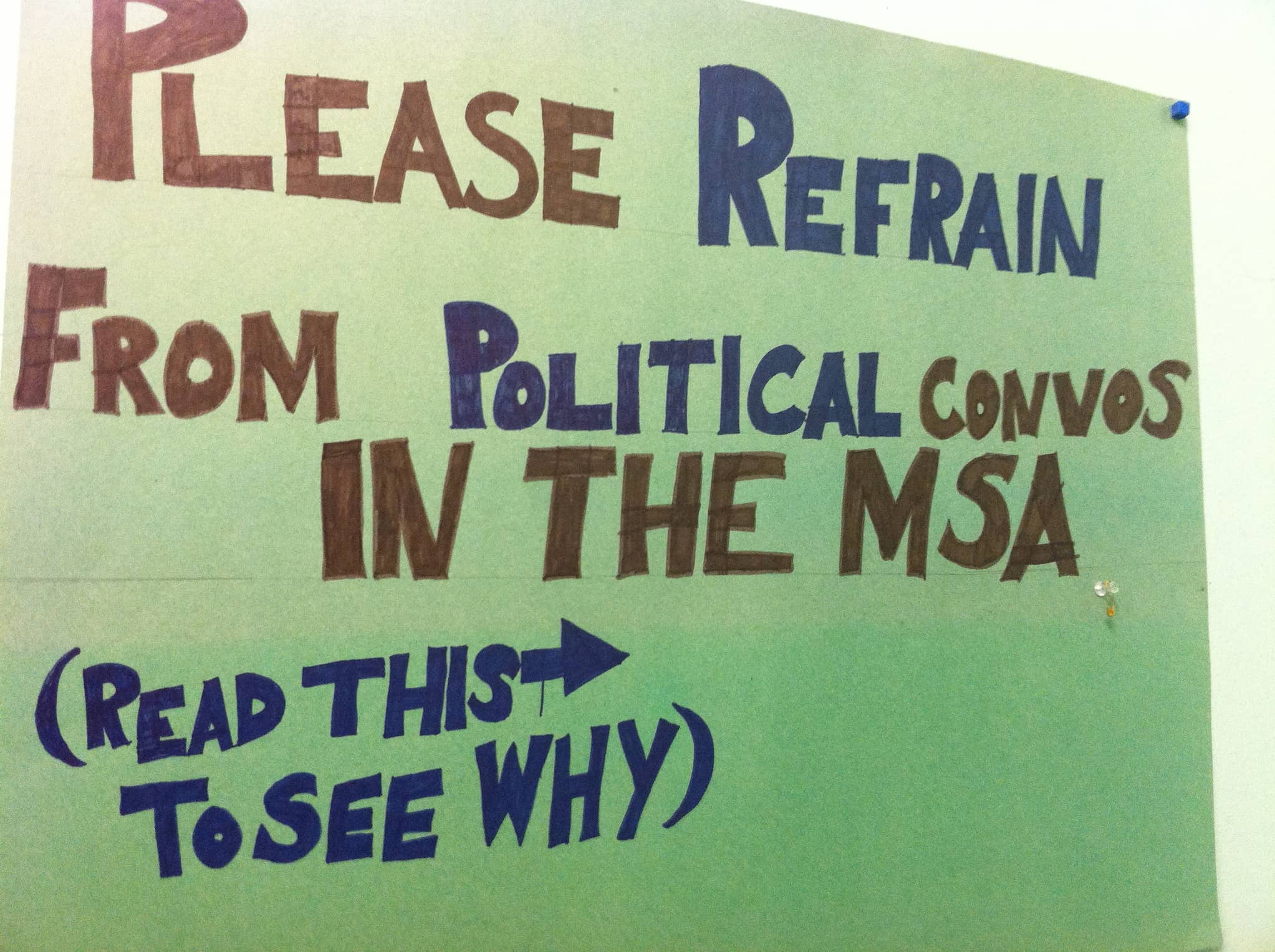 Handwritten sign with capitalized block letters reads, "Please refrain from political convos in the MSA (read this to see why)."