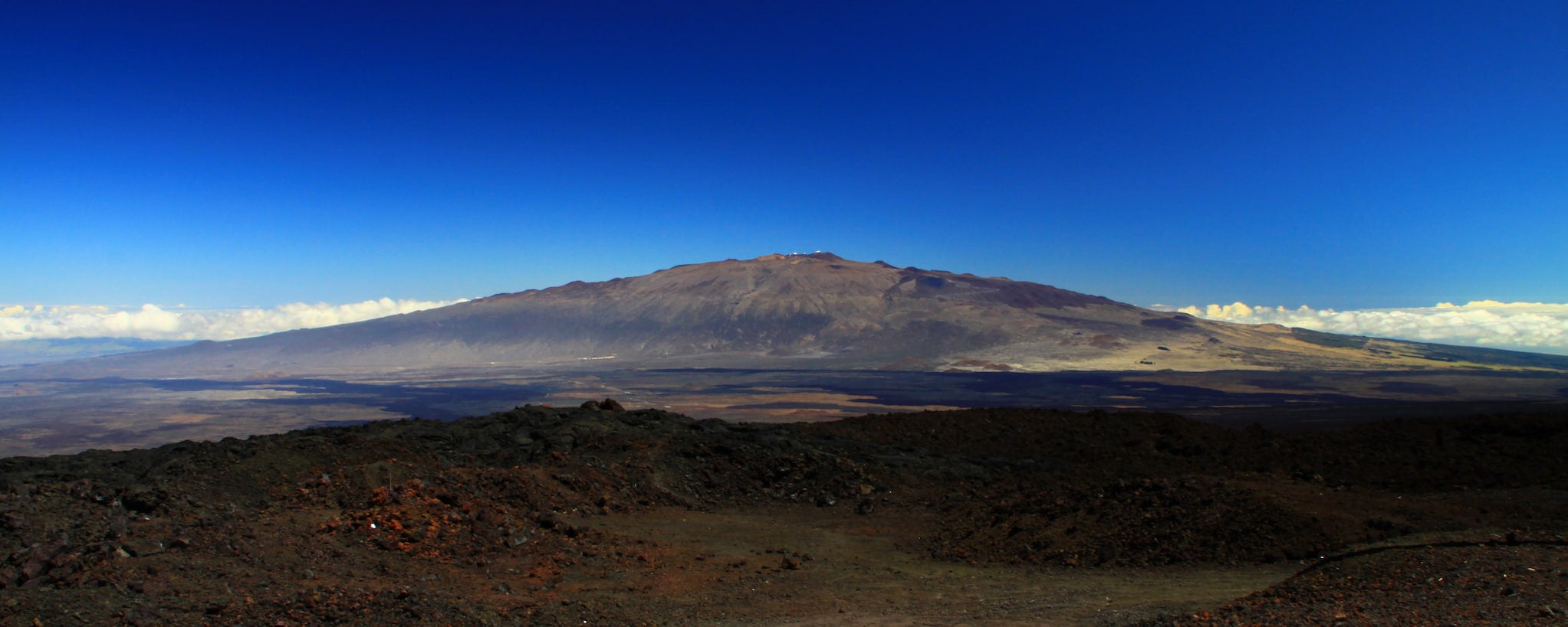 A deep blue sky contrasts with the barren landscape in the foreground of Maunakea.